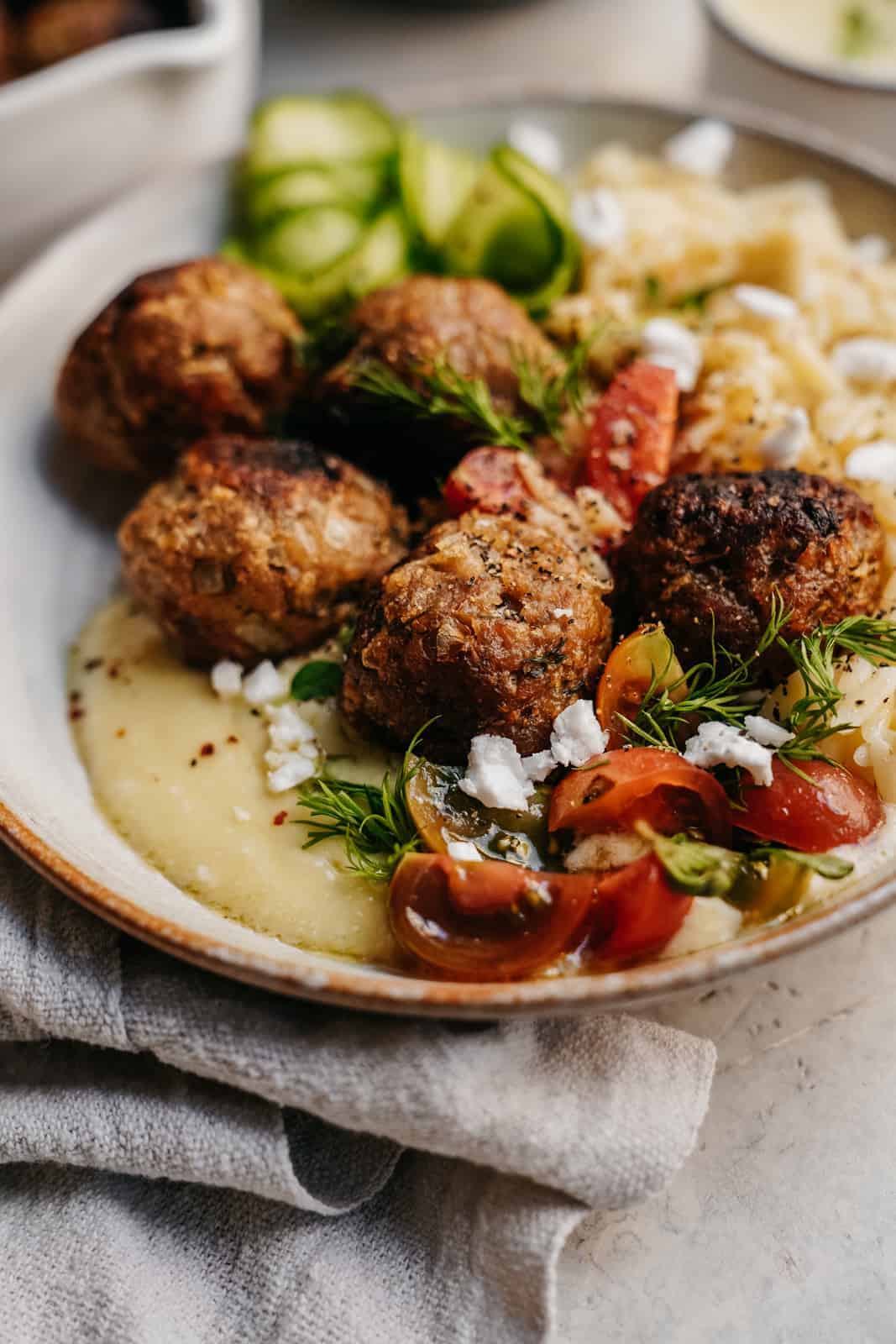 Close-up of Greek meatballs on a dish with creamy hummus and fresh herbs.