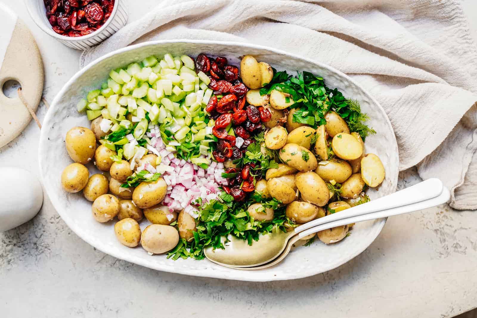 Serving dish with an unmixed potato salad ready to eat with fresh herbs and cranberries.