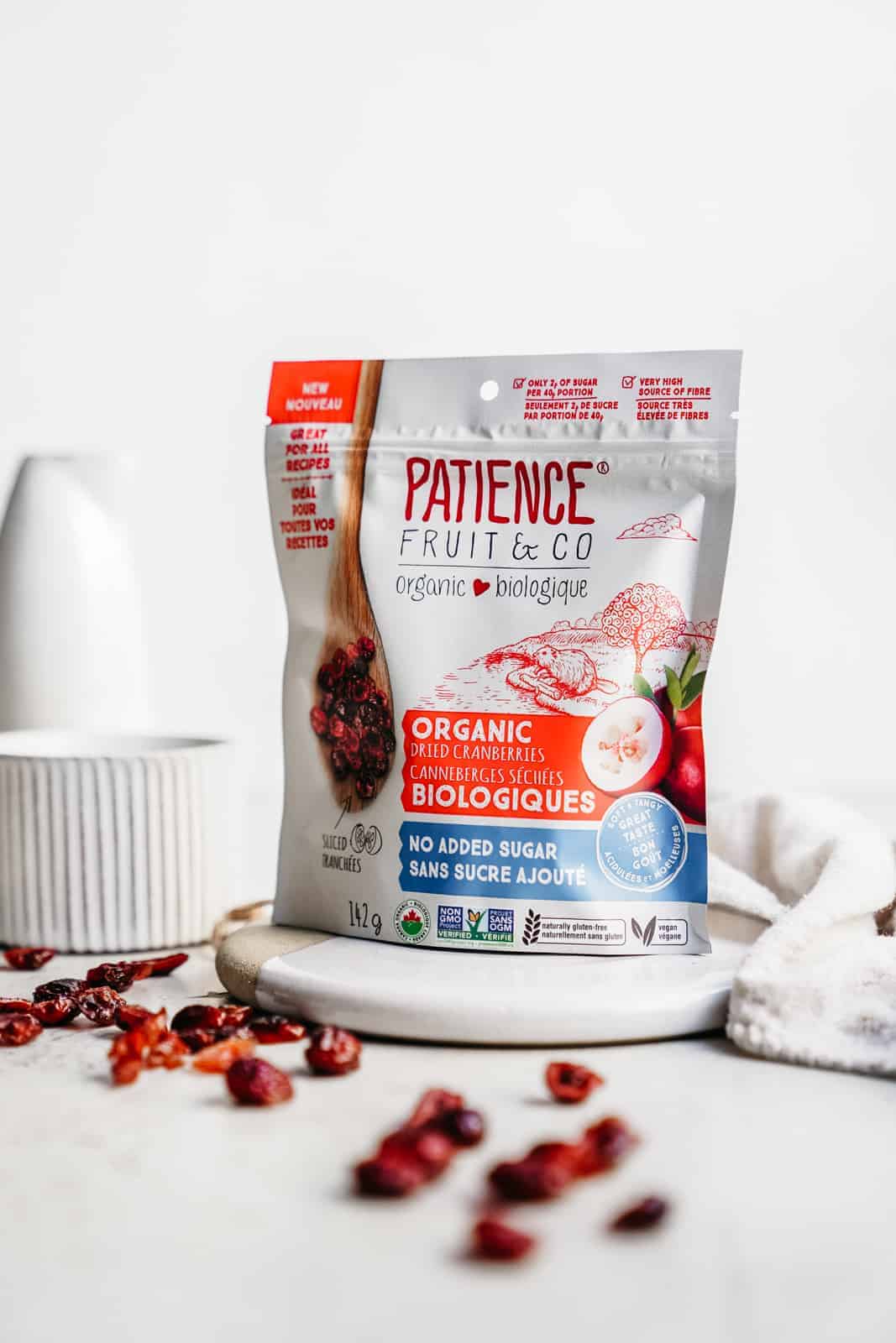 Bag of Patience Fruit & Co. dried cranberries on countertop with some cranberries scattered across counter.