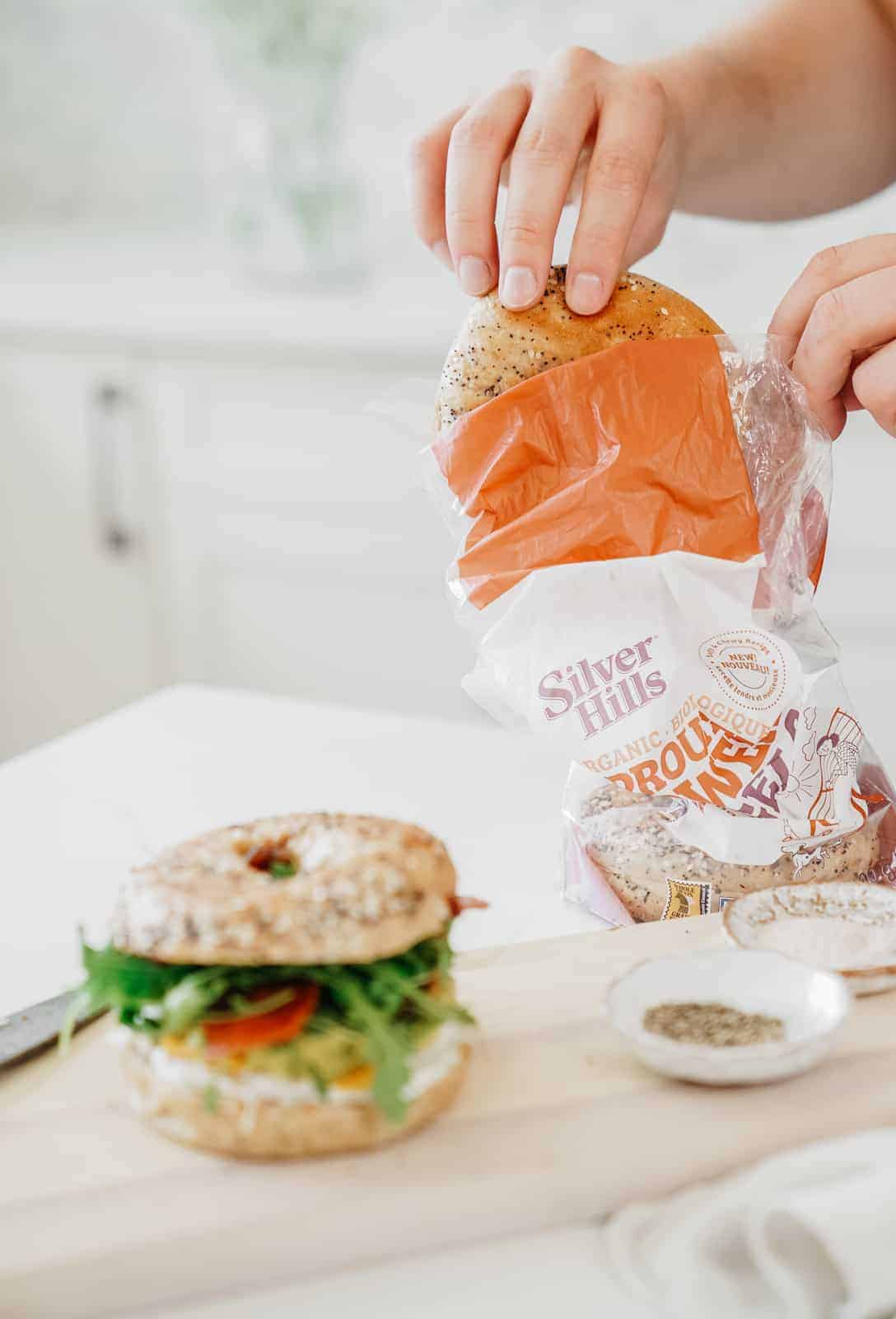 Hand pulling bagel out of bag for a Bagel Sandwich Recipe