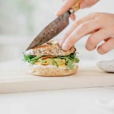 Yummy loaded vegan everything bagel sandwich being cut by a knife for serving.