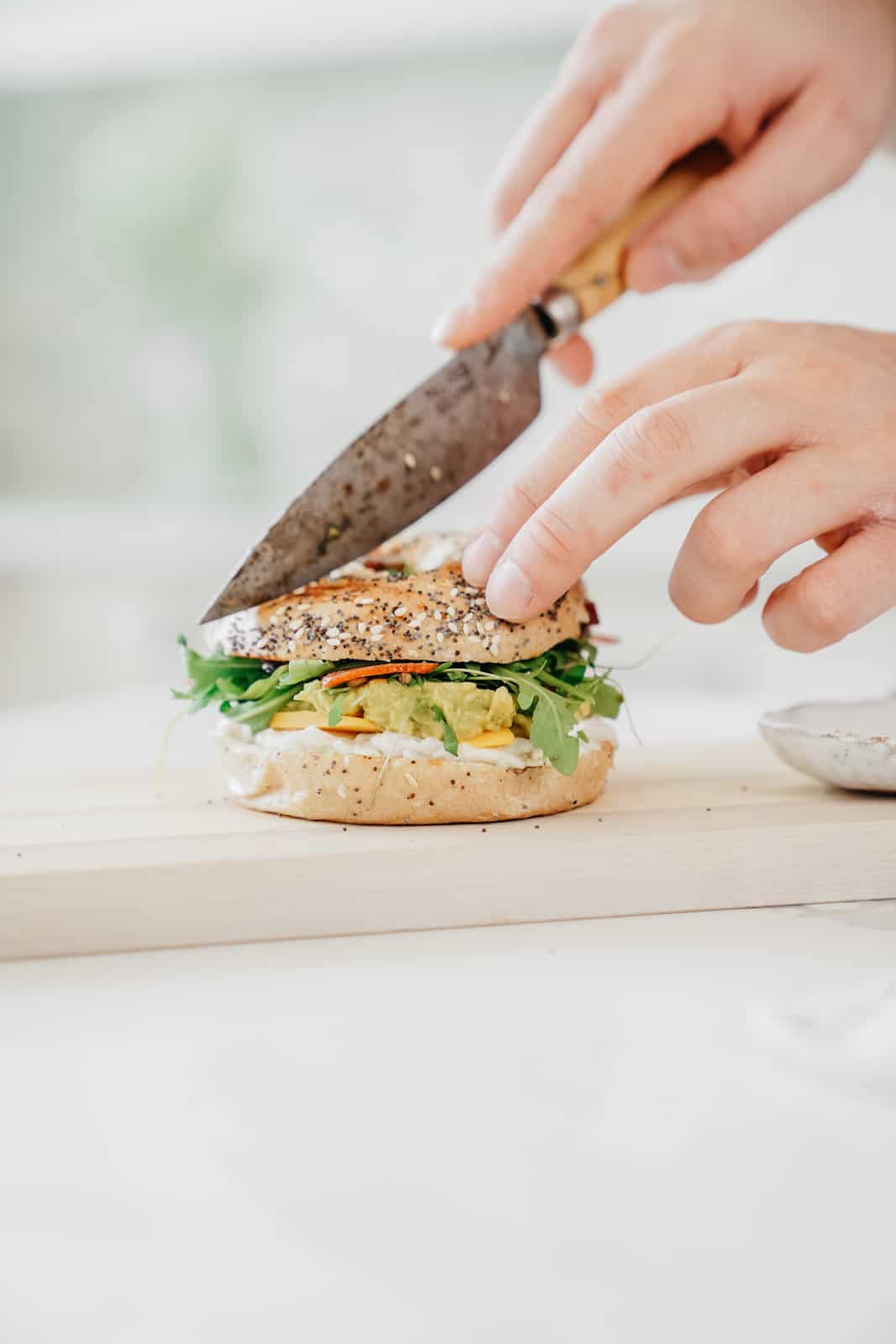 Yummy loaded vegan everything bagel sandwich being cut by a knife for serving.