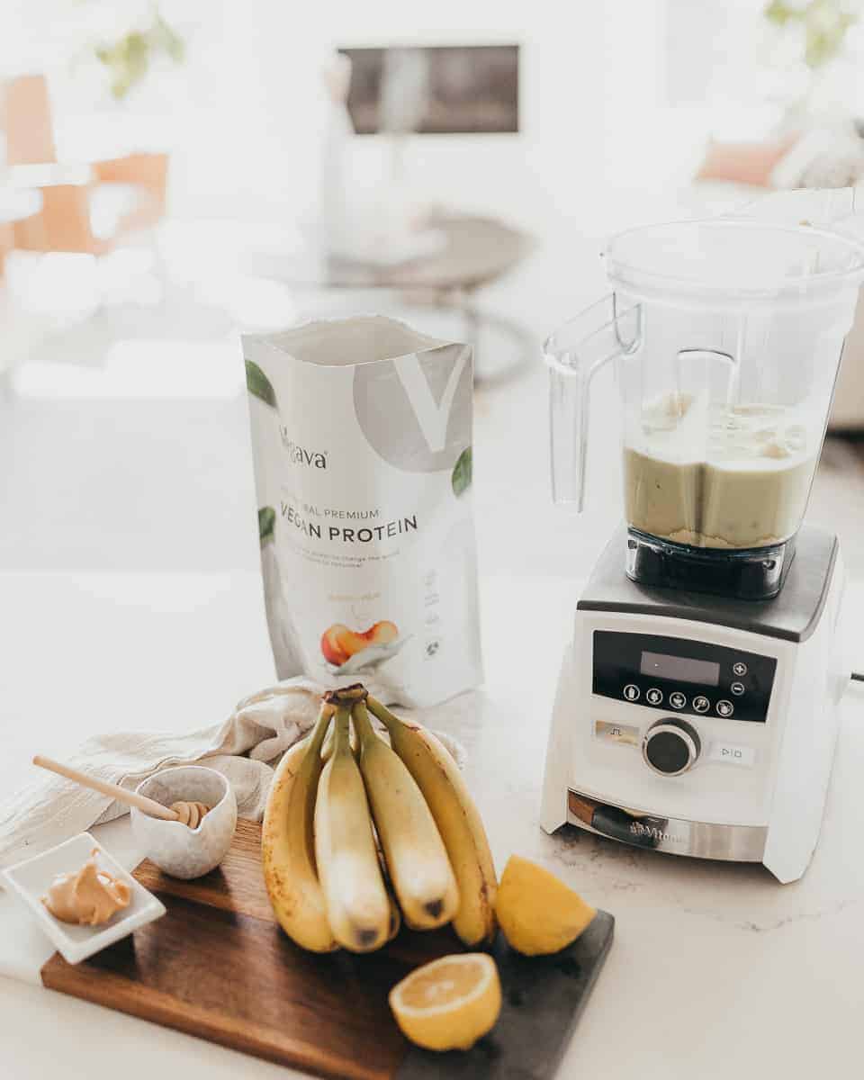 Vegava Protein Powder beside a blender with the other smoothie ingredients at the forefront.