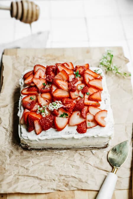 Drizzling honey on top of a Honey Cake that is topped with fresh cut strawberries.