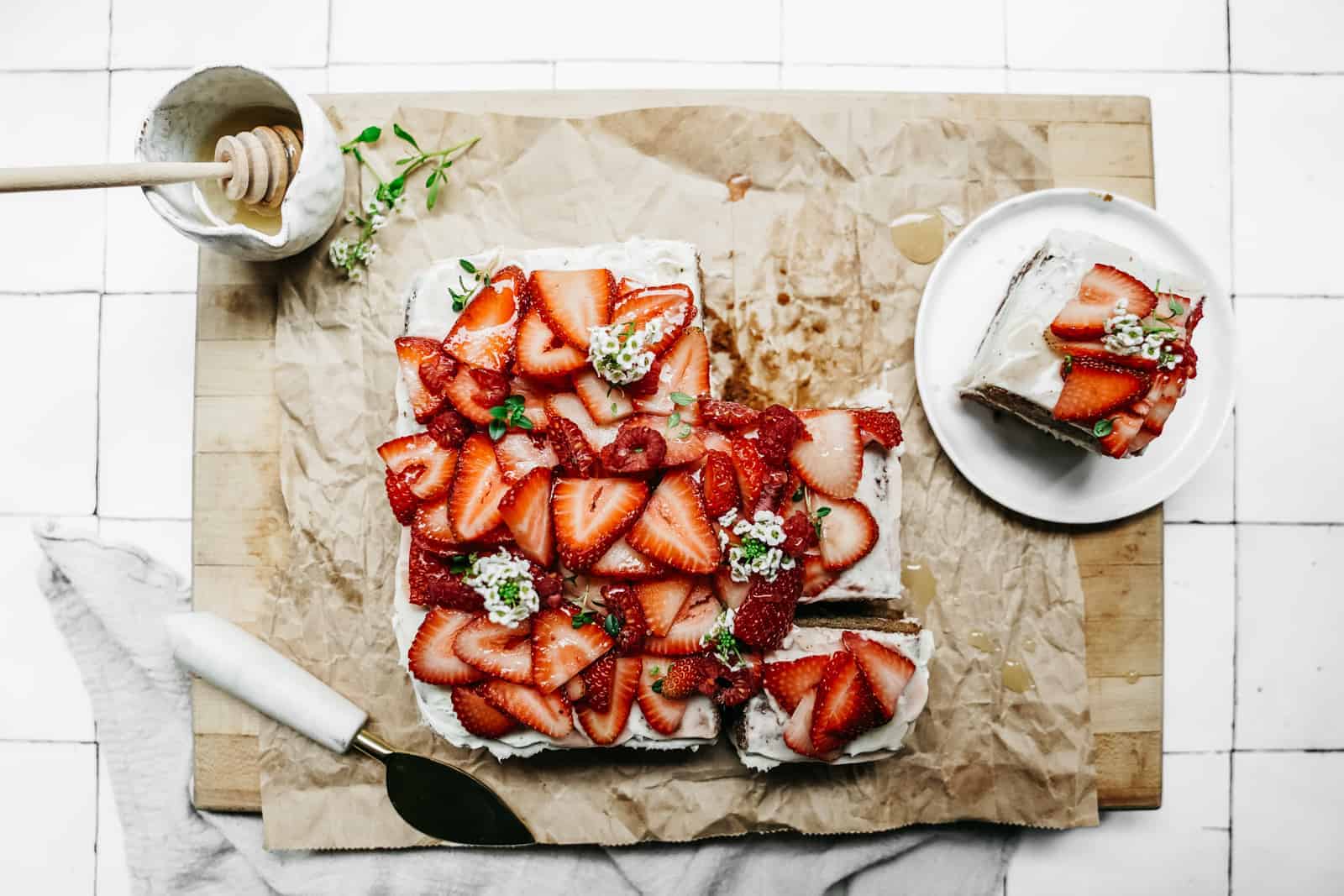 Yummy spring Honey Cake sitting on a cutting board with fresh strawberries sliced on top.