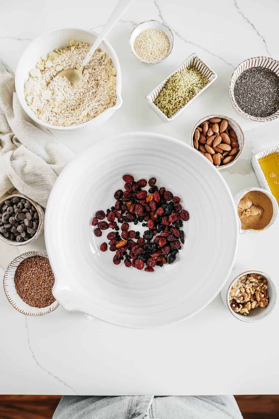 Ingredients for Vegan Granola Bars Recipe laid out on a table with juicy dried cranberries in the centre.