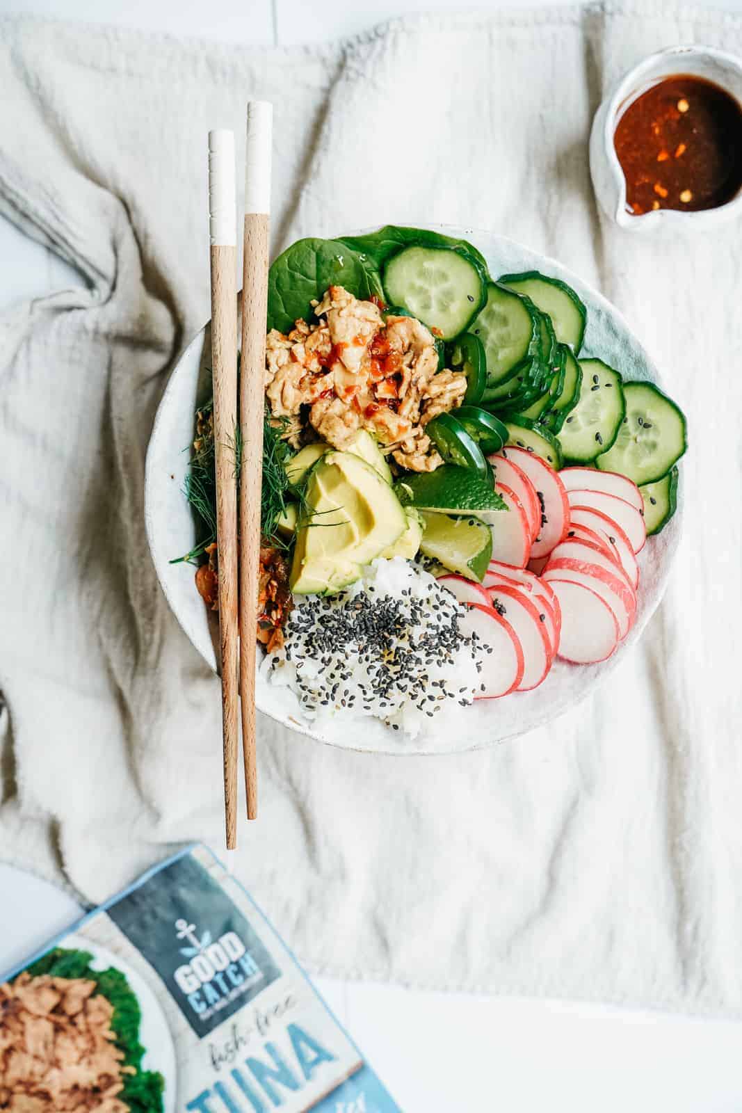 Vegan Tuna Poke Bowl sitting on white blanket with chilli sauce & Good Catch Foods Tuna in background.