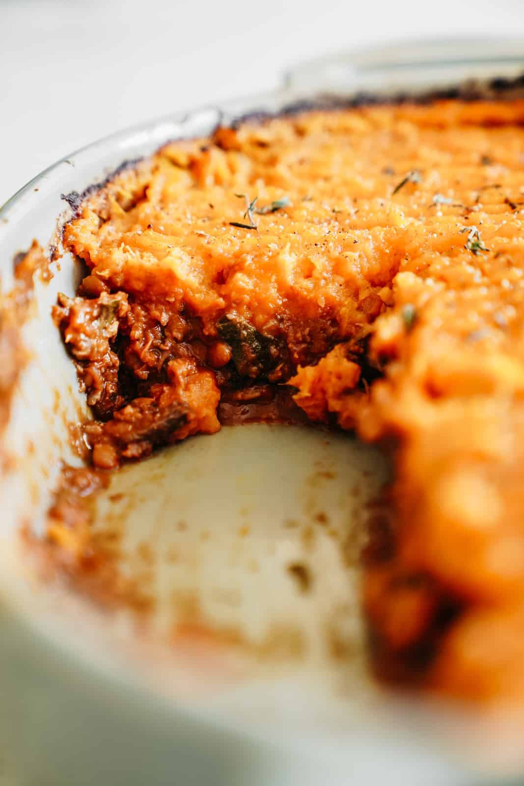 A close-up of a casserole dish with Vegan Shepherd's Pie with a slice removed.