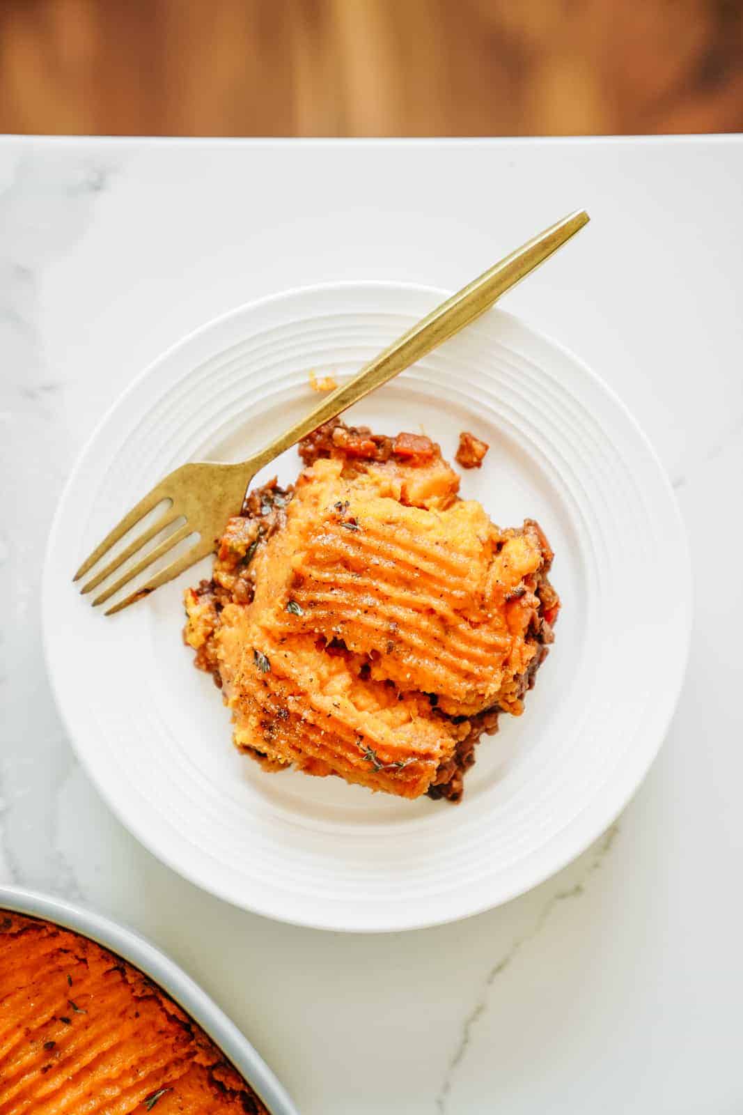 A slice of Vegan Shepherd's Pie sitting on white plate with gold fork.