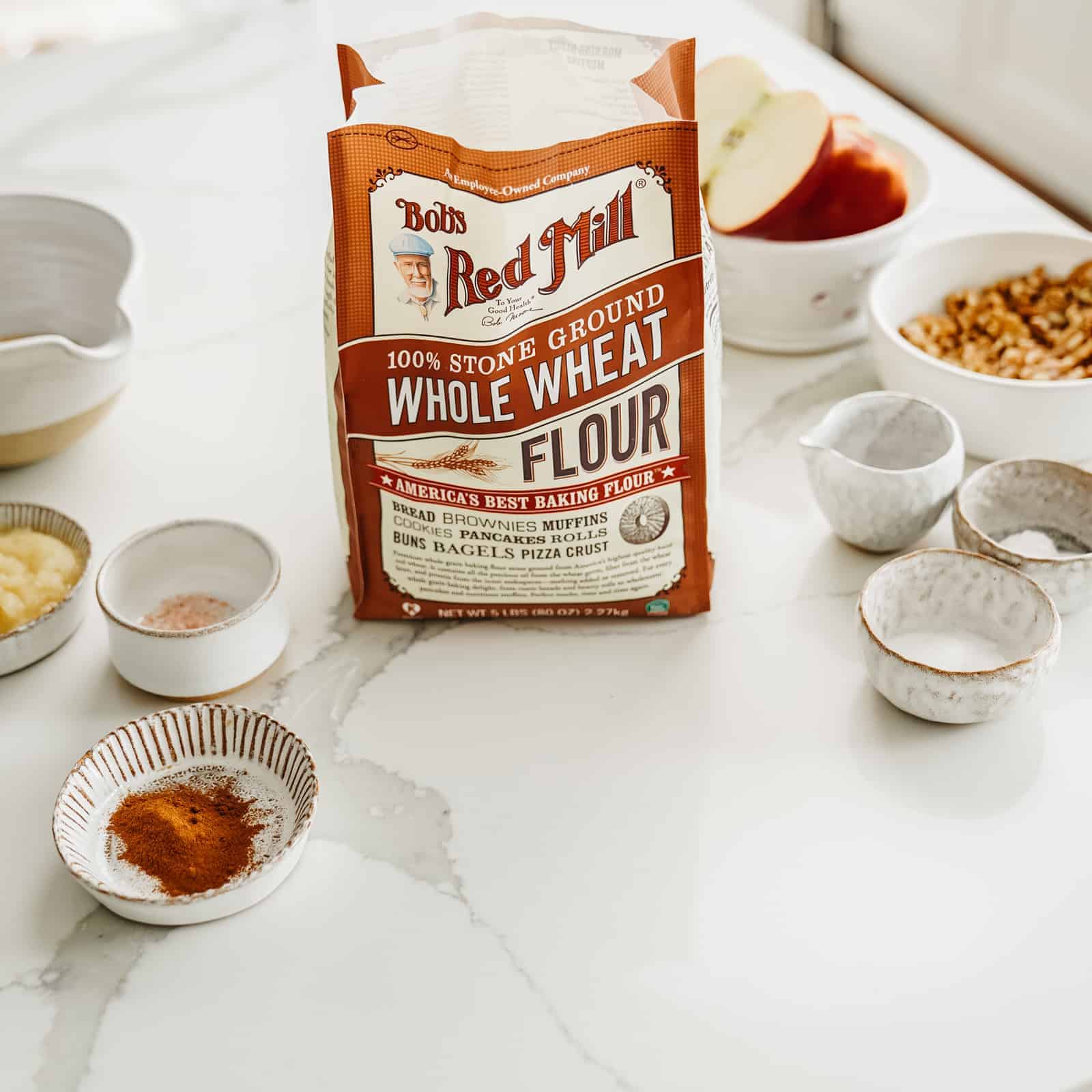 Bag of Bob's Red Mill Whole Wheat Flour sitting on countertop surrounded by other muffin ingredients.