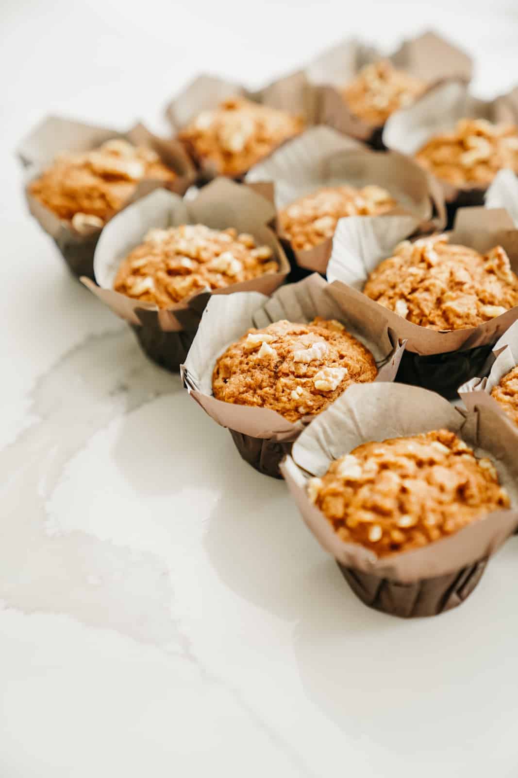 A dozen Vegan Apple Cinnamon Muffins all lined up in muffin wrappers on counter.