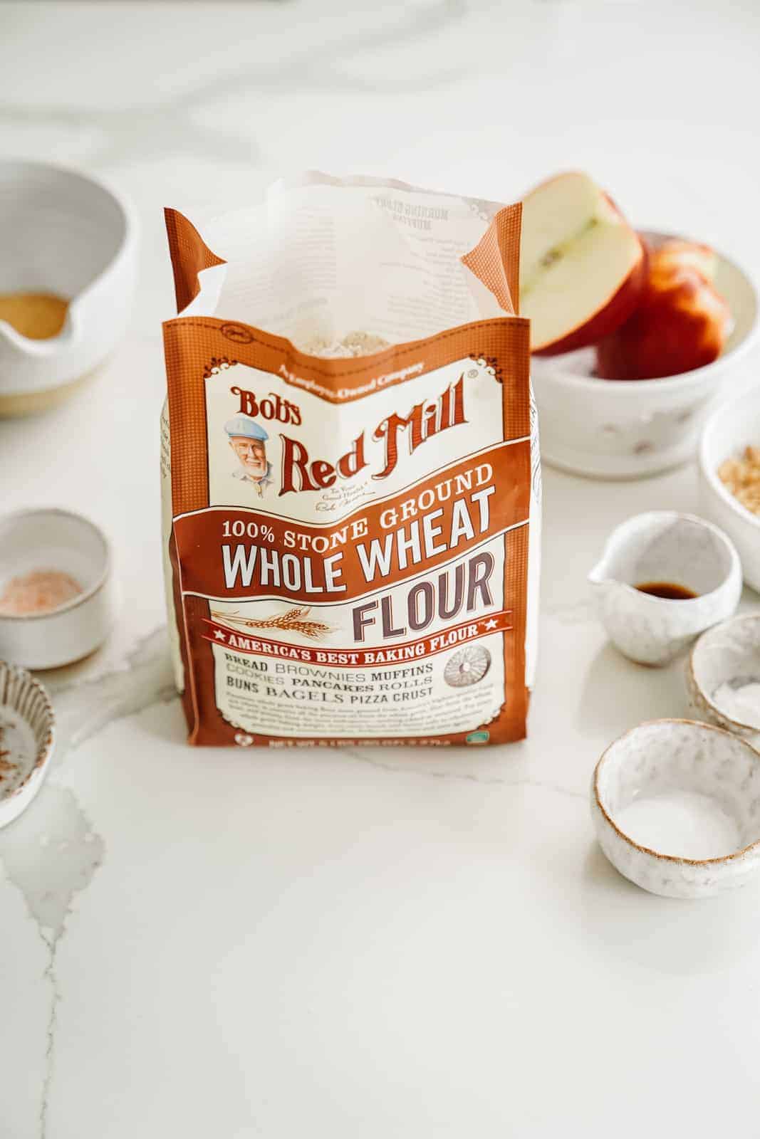 Bag of Bob's Red Mill Whole Wheat Flour sitting on countertop surrounded by other muffin ingredients.