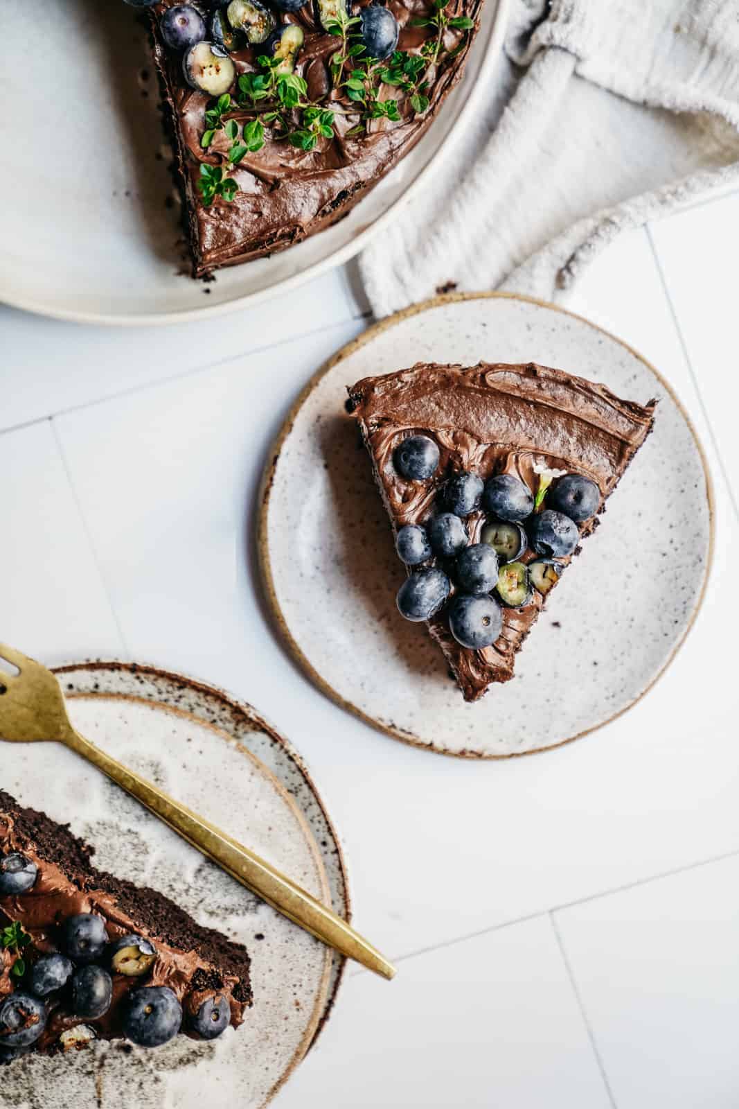 Slices of Vegan Chocolate Cake recipe scattered on white plates on the countertop.