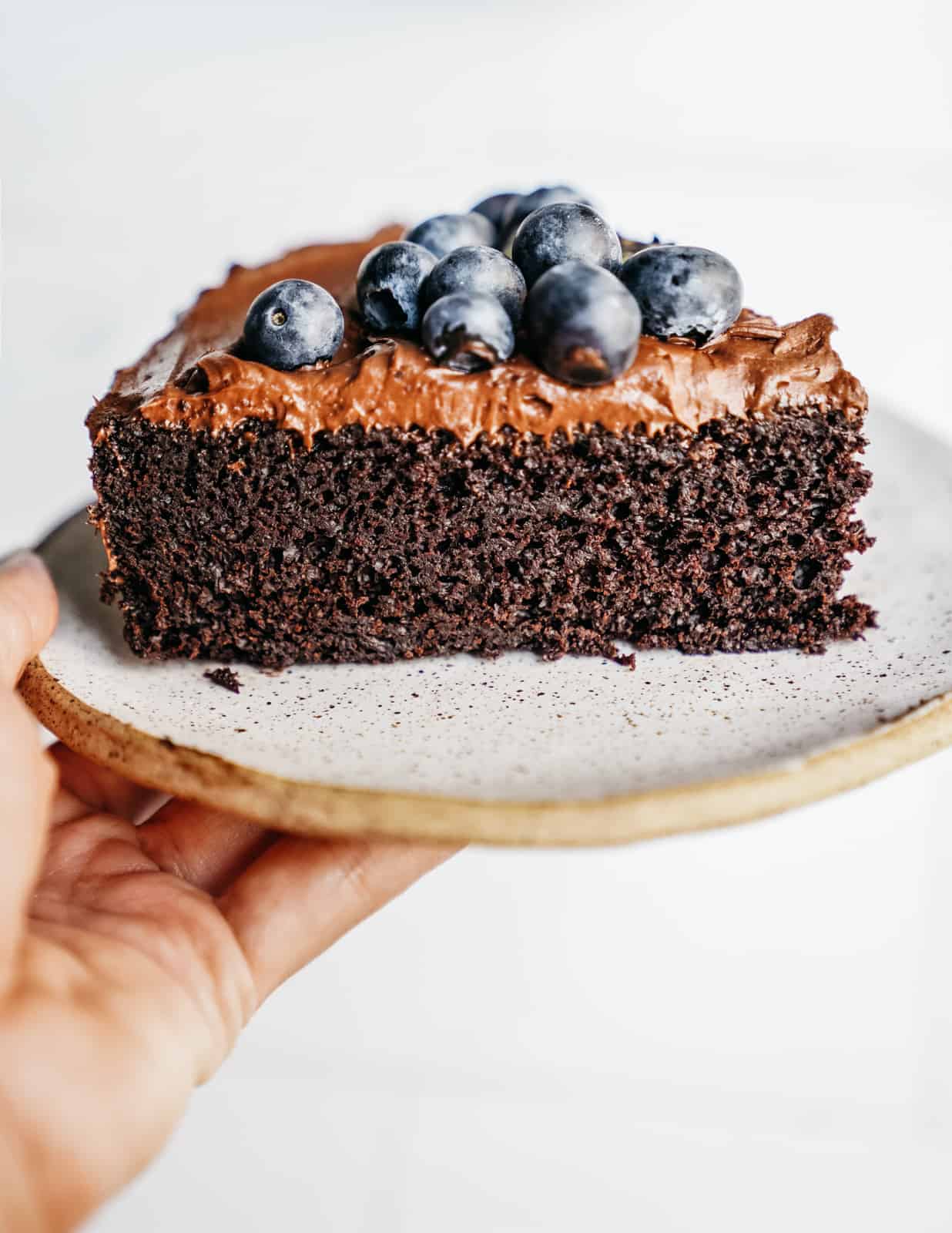 Close-up of a slice of moist Easy Vegan Chocolate Cake recipe garnished with cashew frosting and blueberries.