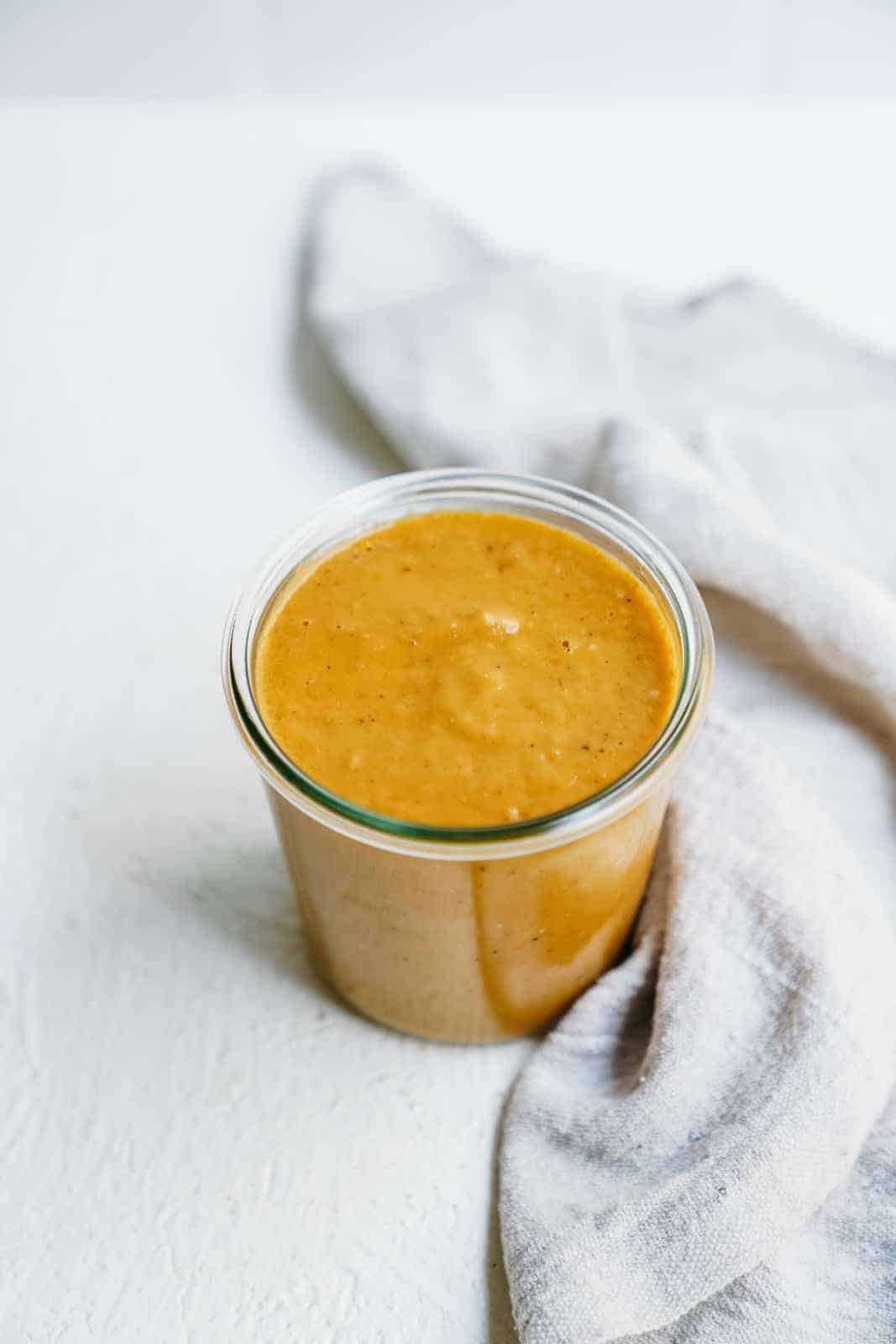 Jar of tomatillo dressing on white countertop beside a napkin.