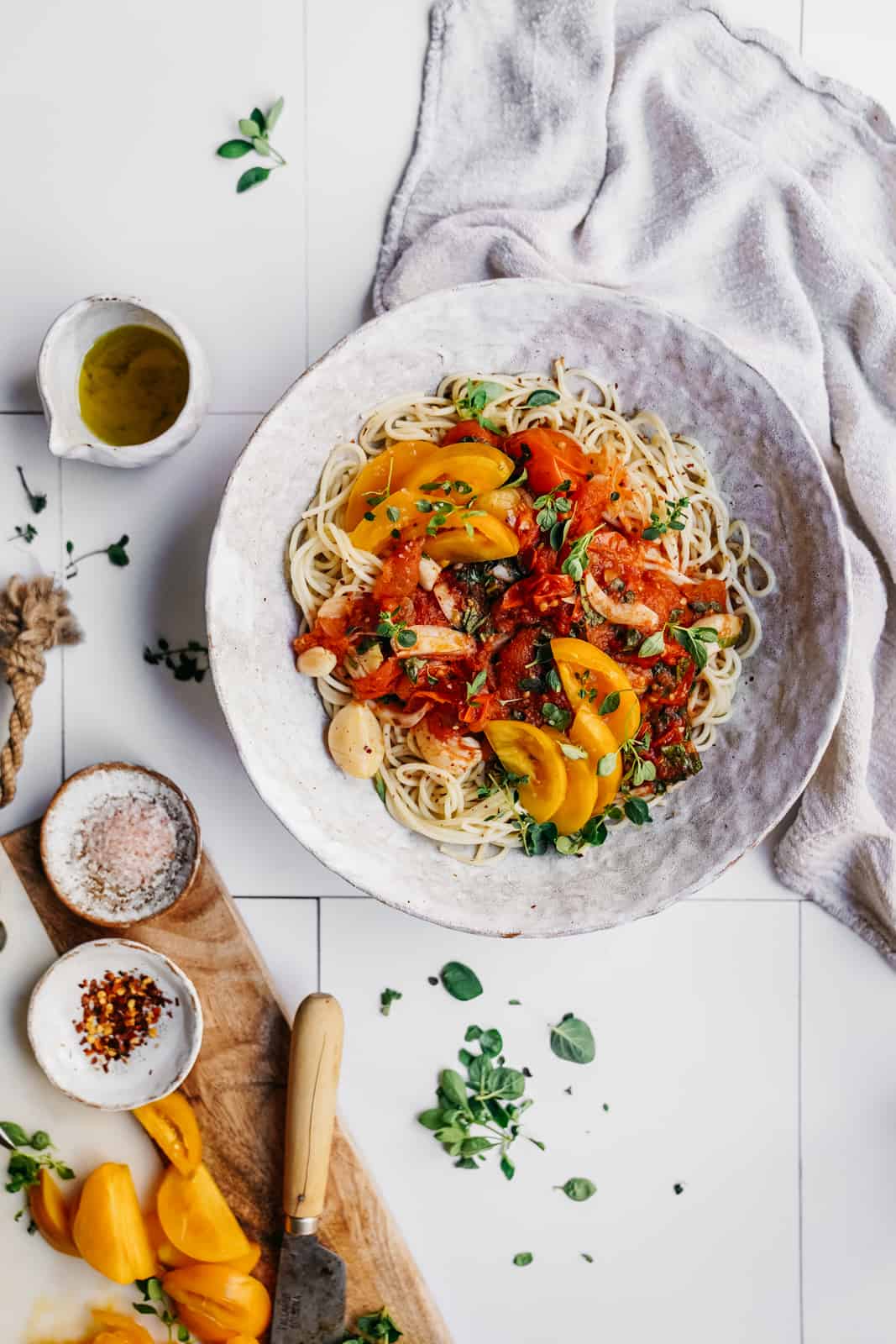 Big white bowl of Tomato and Garlic Pasta on a counter surrounded by little bowls of fresh ingredients.