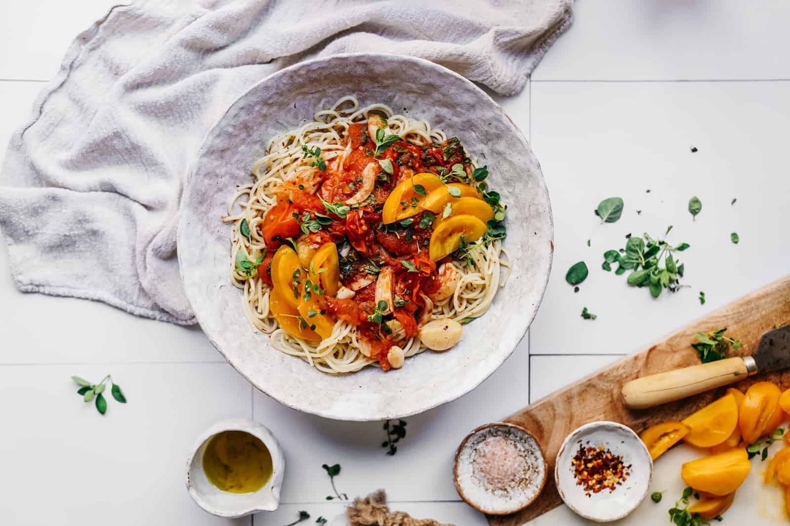 Big white bowl of Tomato and Garlic Pasta on a counter surrounded by little bowls of fresh ingredients. 