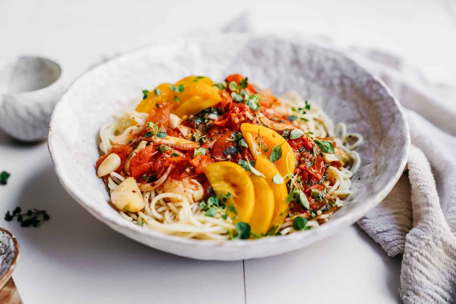 Big white bowl of Tomato and Garlic Pasta on a counter with cloth behind it.