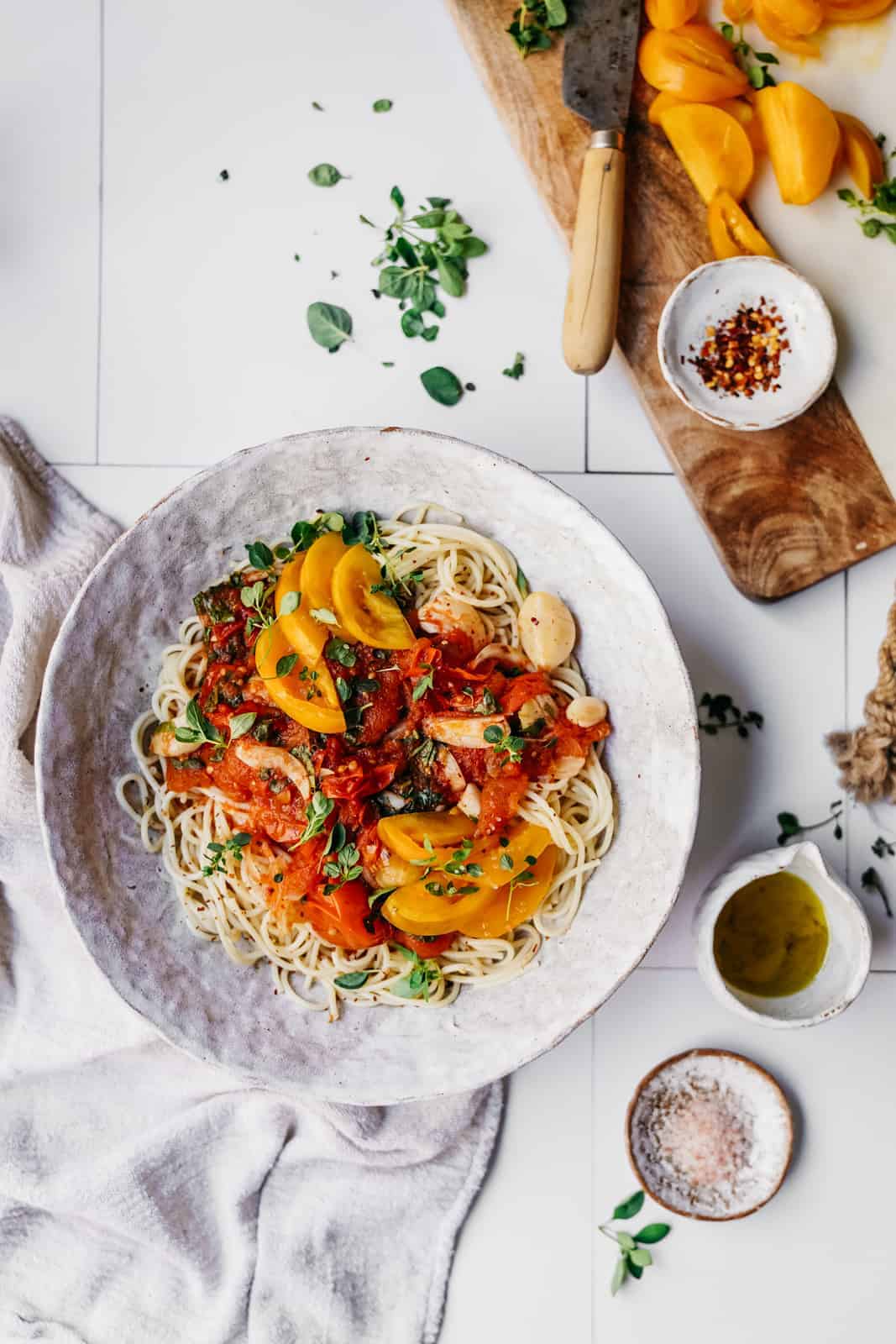 Big white bowl of Tomato and Garlic Pasta on a counter surrounded by little bowls of fresh ingredients.