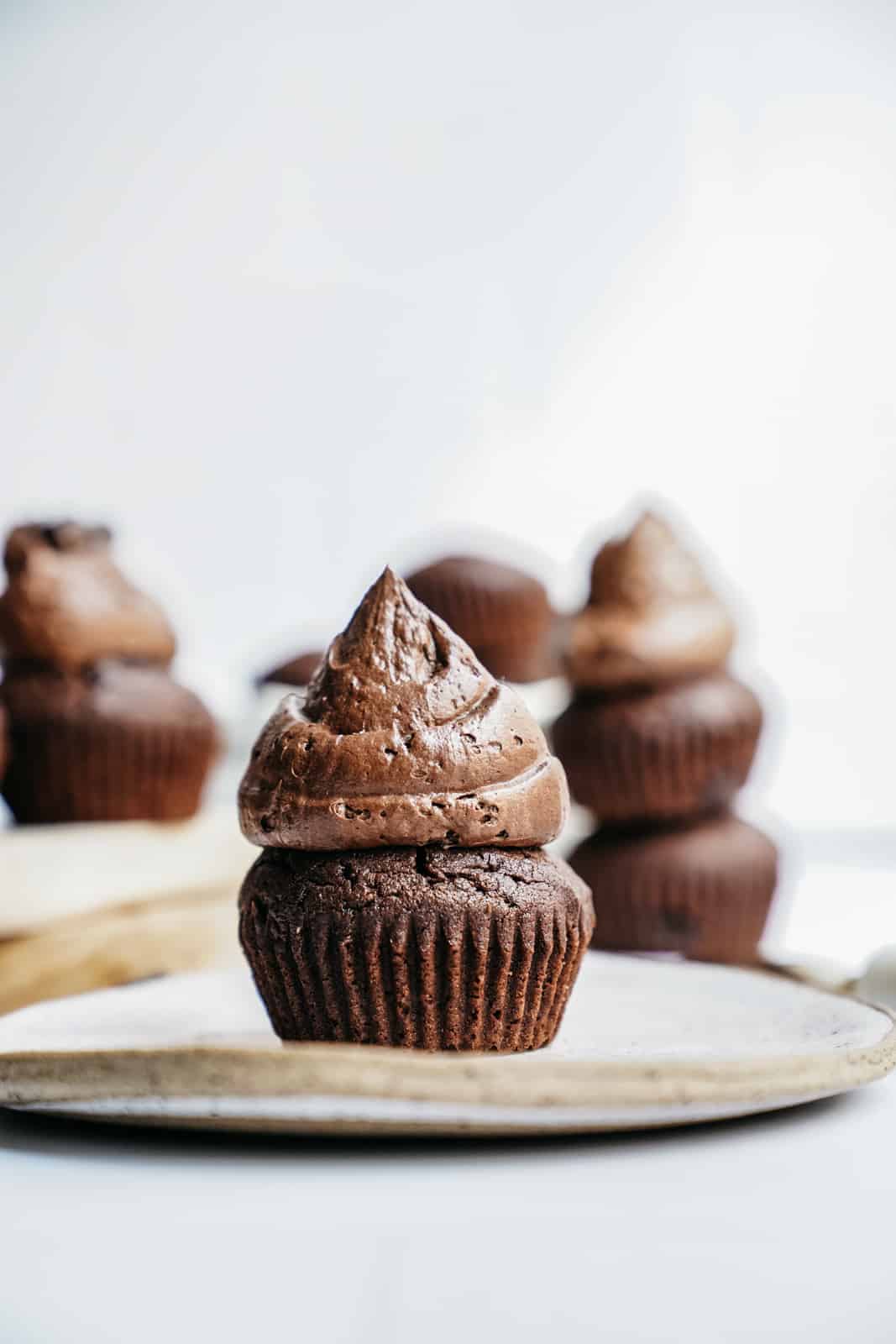 A beautiful chocolate muffin with a big dollop of creamy icing on top sitting on a plate.