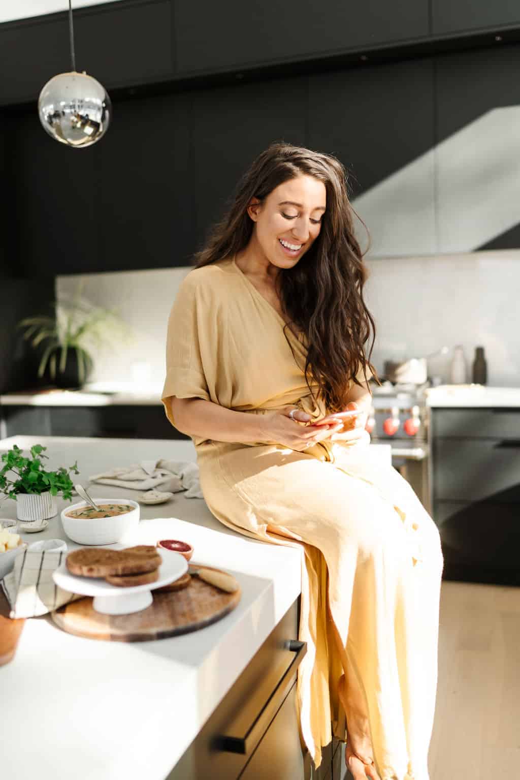 Maria sitting on countertop in kitchen with phone in her hand showing aspiring food bloggers what mistakes they shouldn't be making