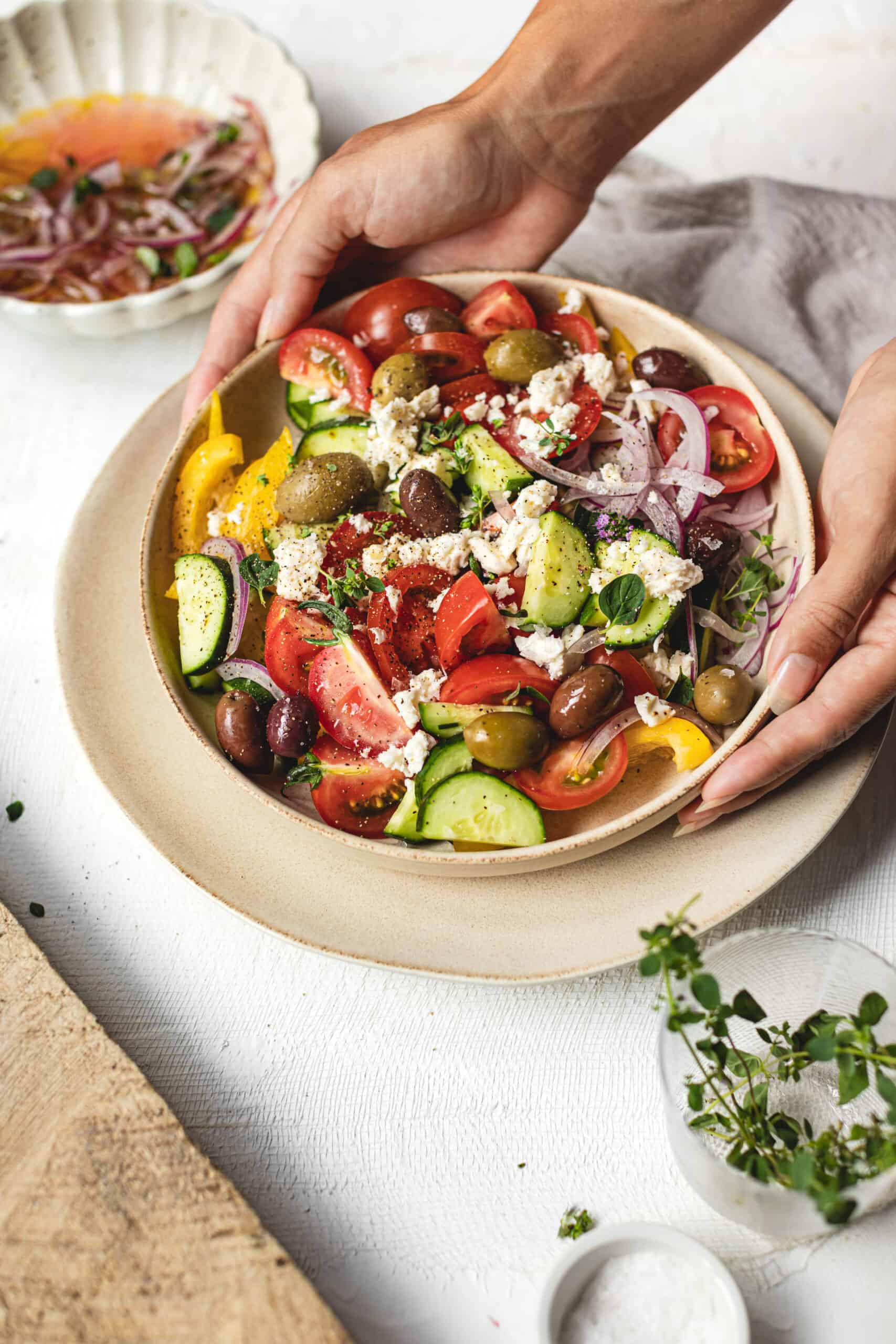 Big colorful bowl of Simple Homemade Greek Salad with hands placing it on table