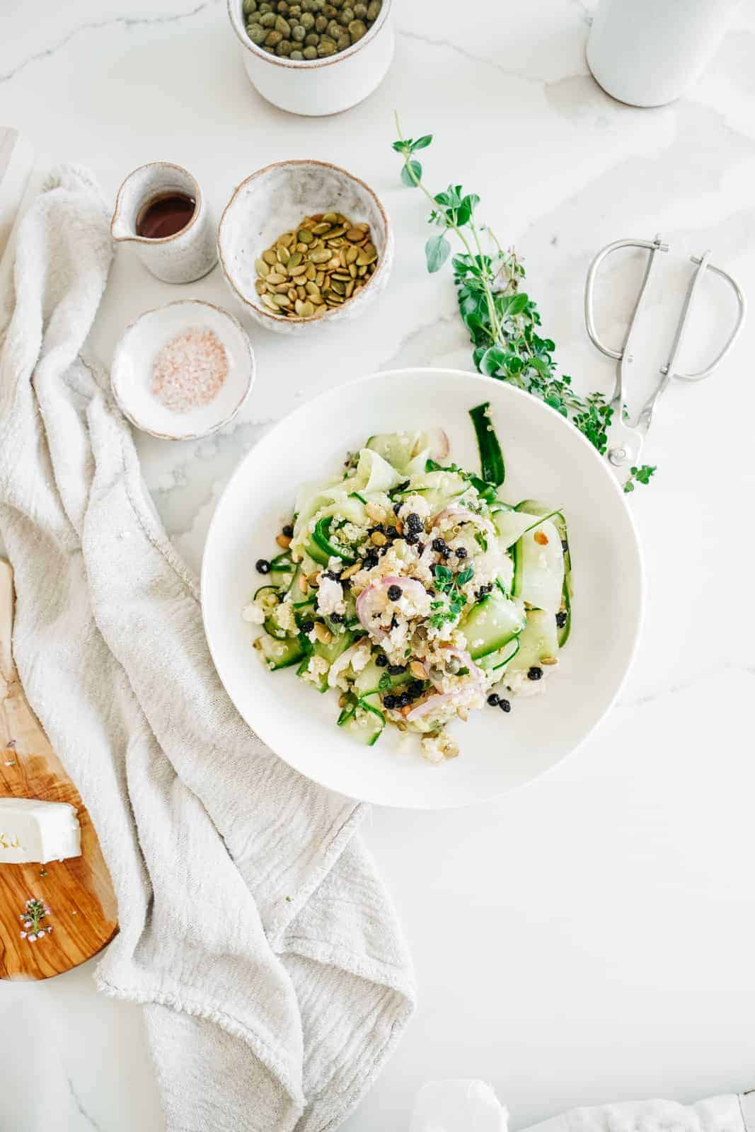 White bowl of Shaved Cucumber Salad with ingredients surrounding it.