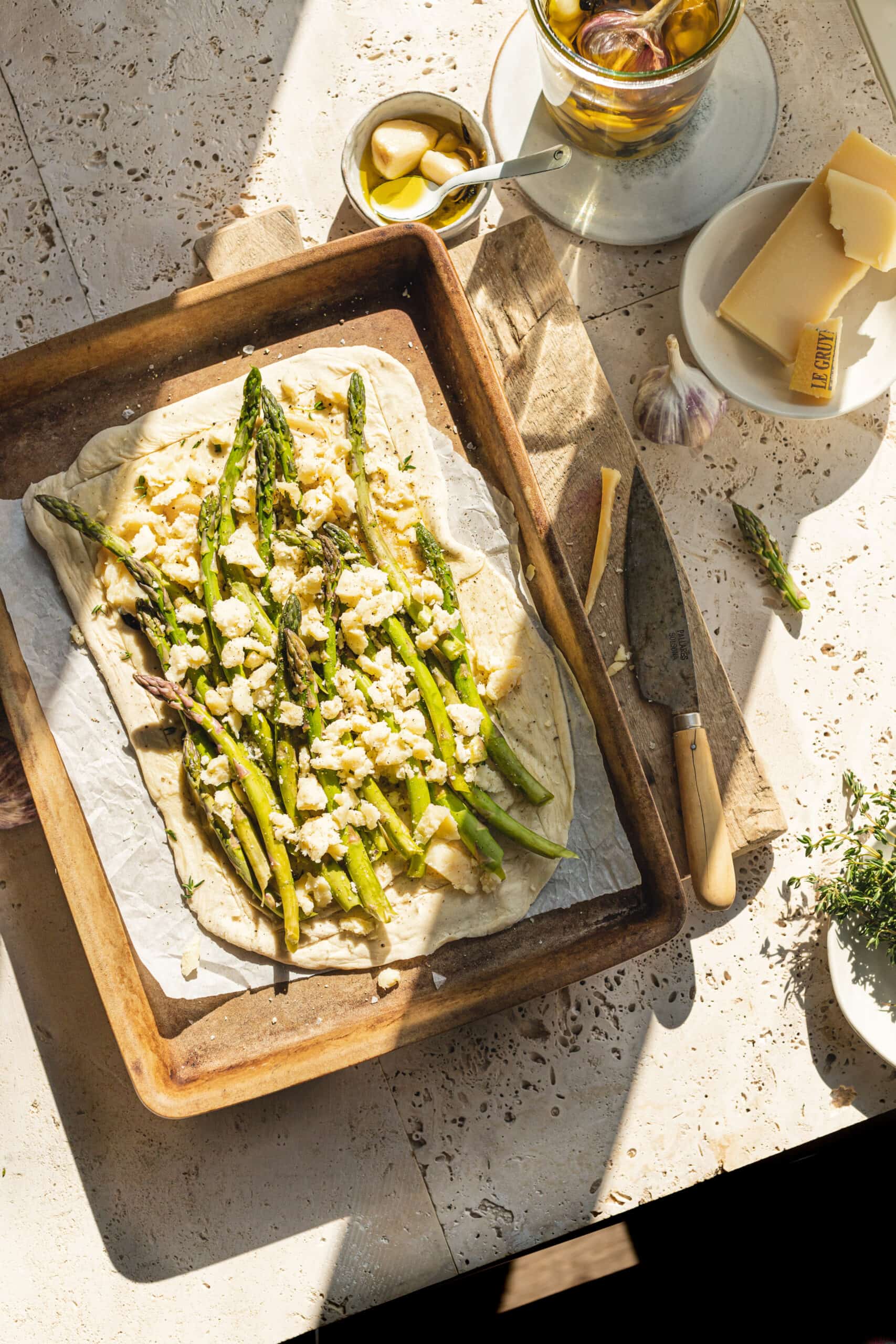 A beautiful Asparagus & Cheese Tart ready to be baked sitting on baking tray with sun shining through window.