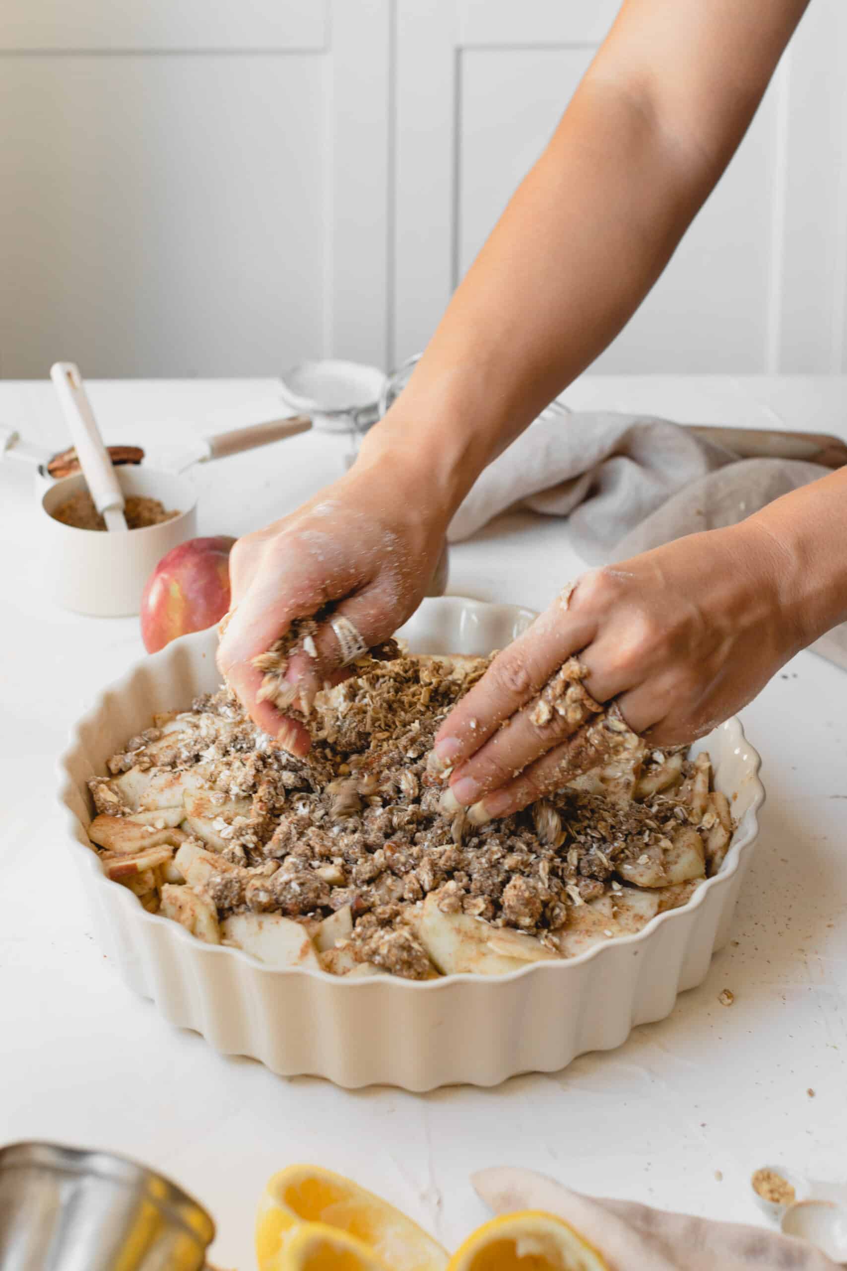 Person sprinkling the crumble on top of the apple in a serving dish.