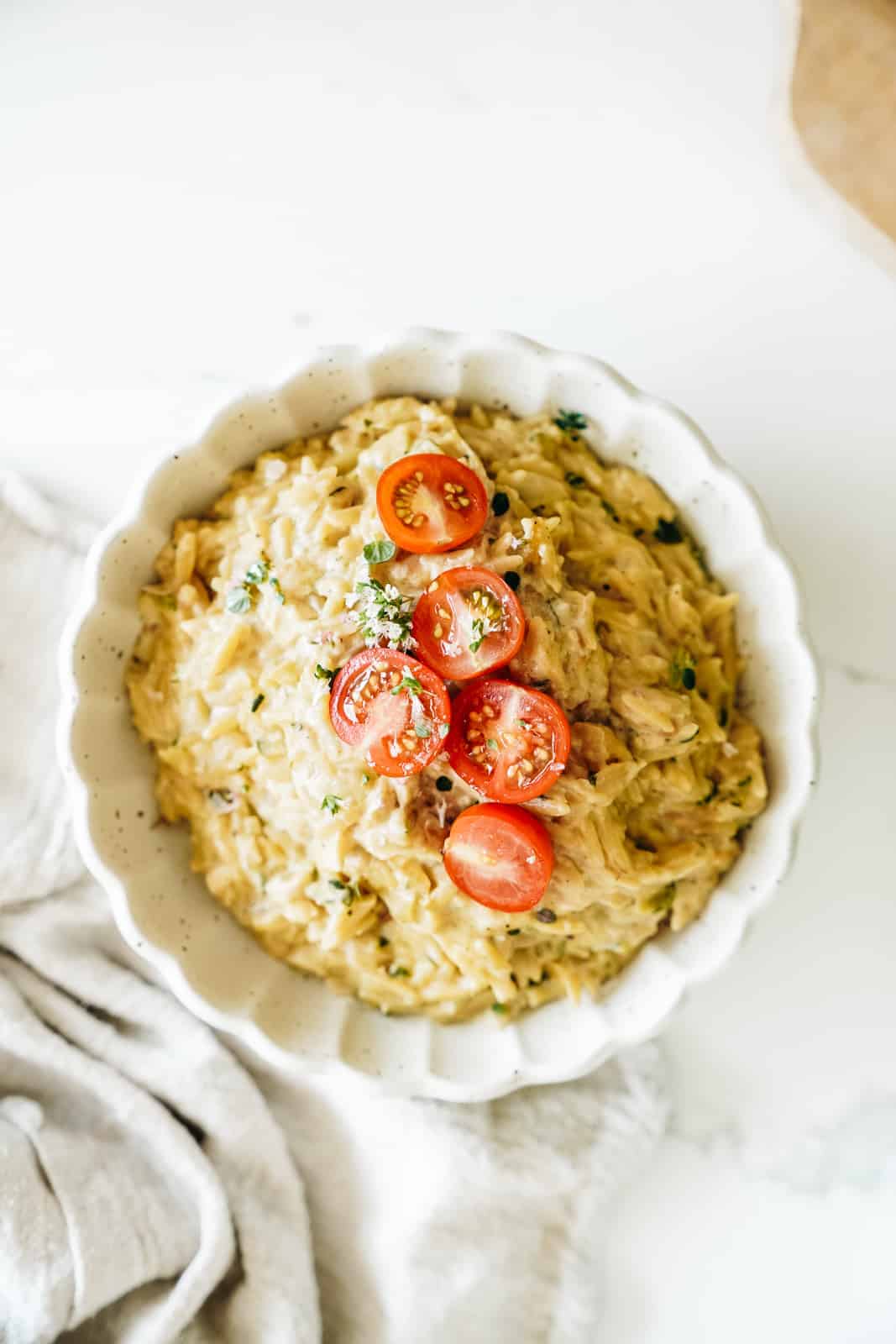 A close up shot a big bowl of Vegan Orzo with Creamy Zucchini and Lemon garnished with tomatoes and herbs