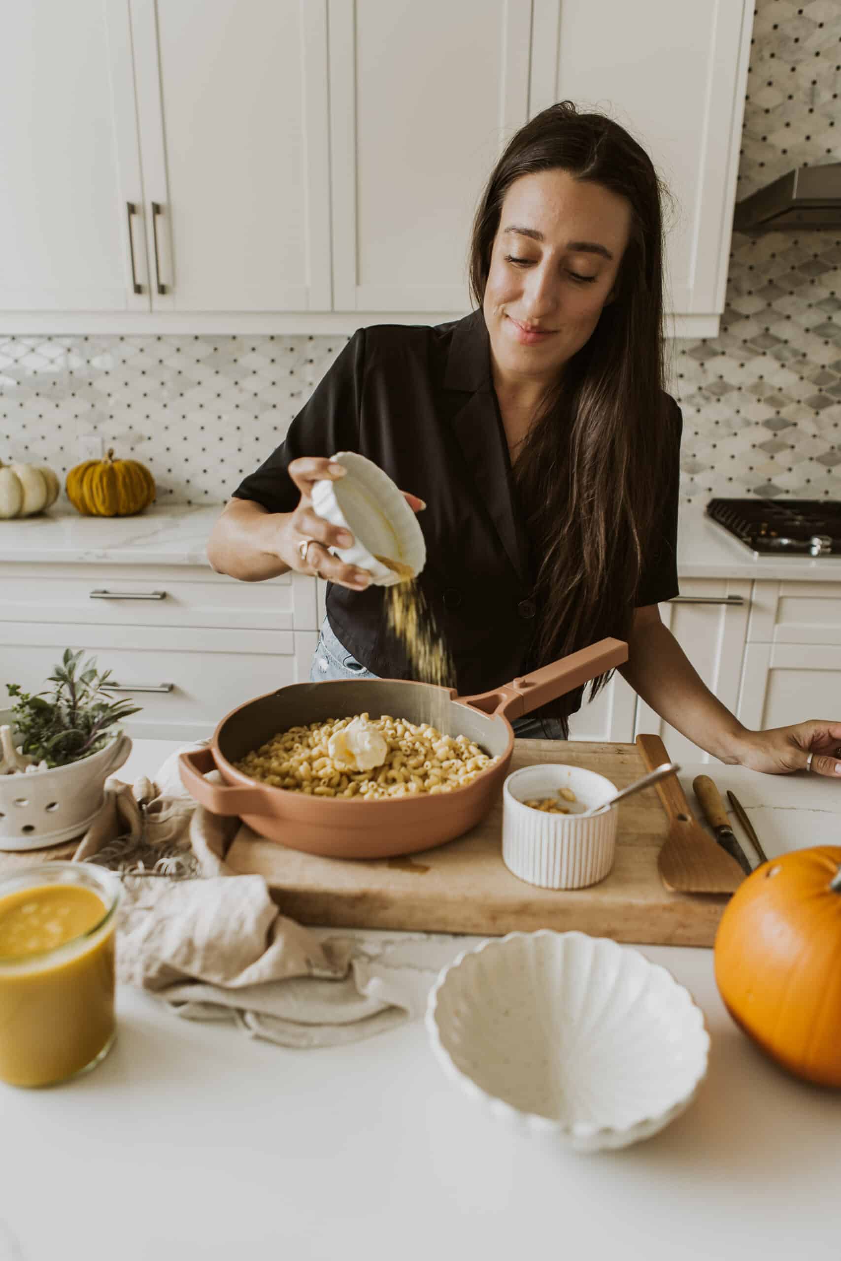 Maria pouring toppings on Vegan Pumpkin Mac and Cheese