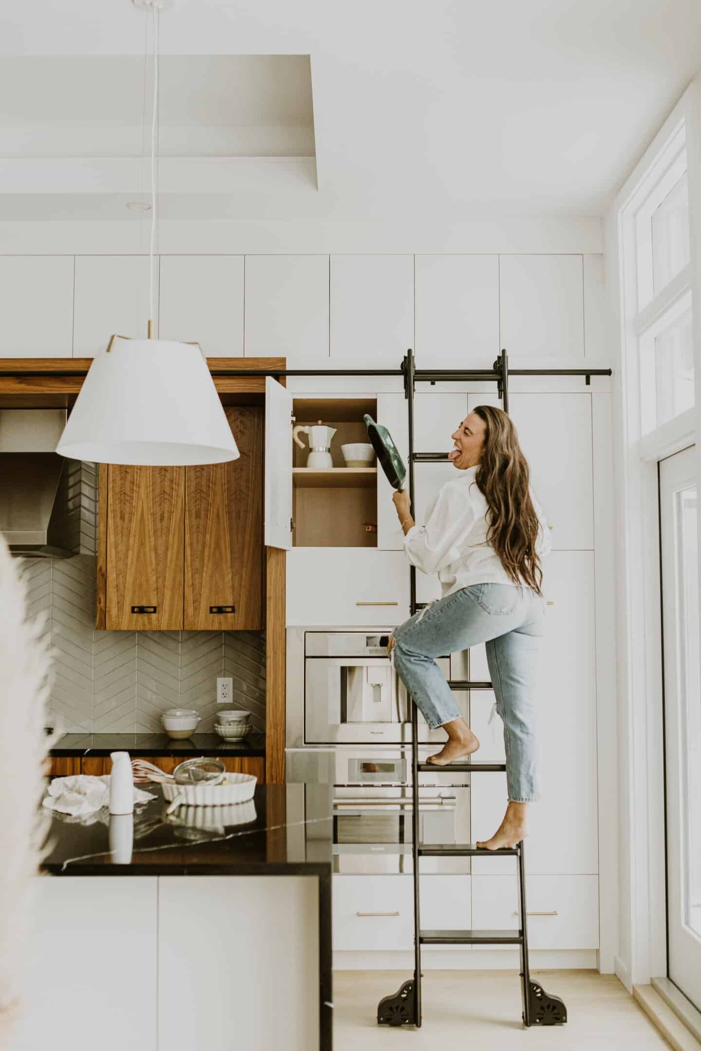 Food blogger, Maria, climbing a ladder in a kitchen to reach a pan.