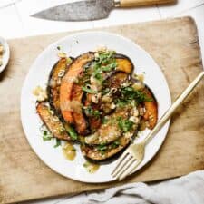 Roasted acorn squash on a white plate on a cutting board.