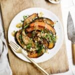 Roasted acorn squash on a white plate on a cutting board.