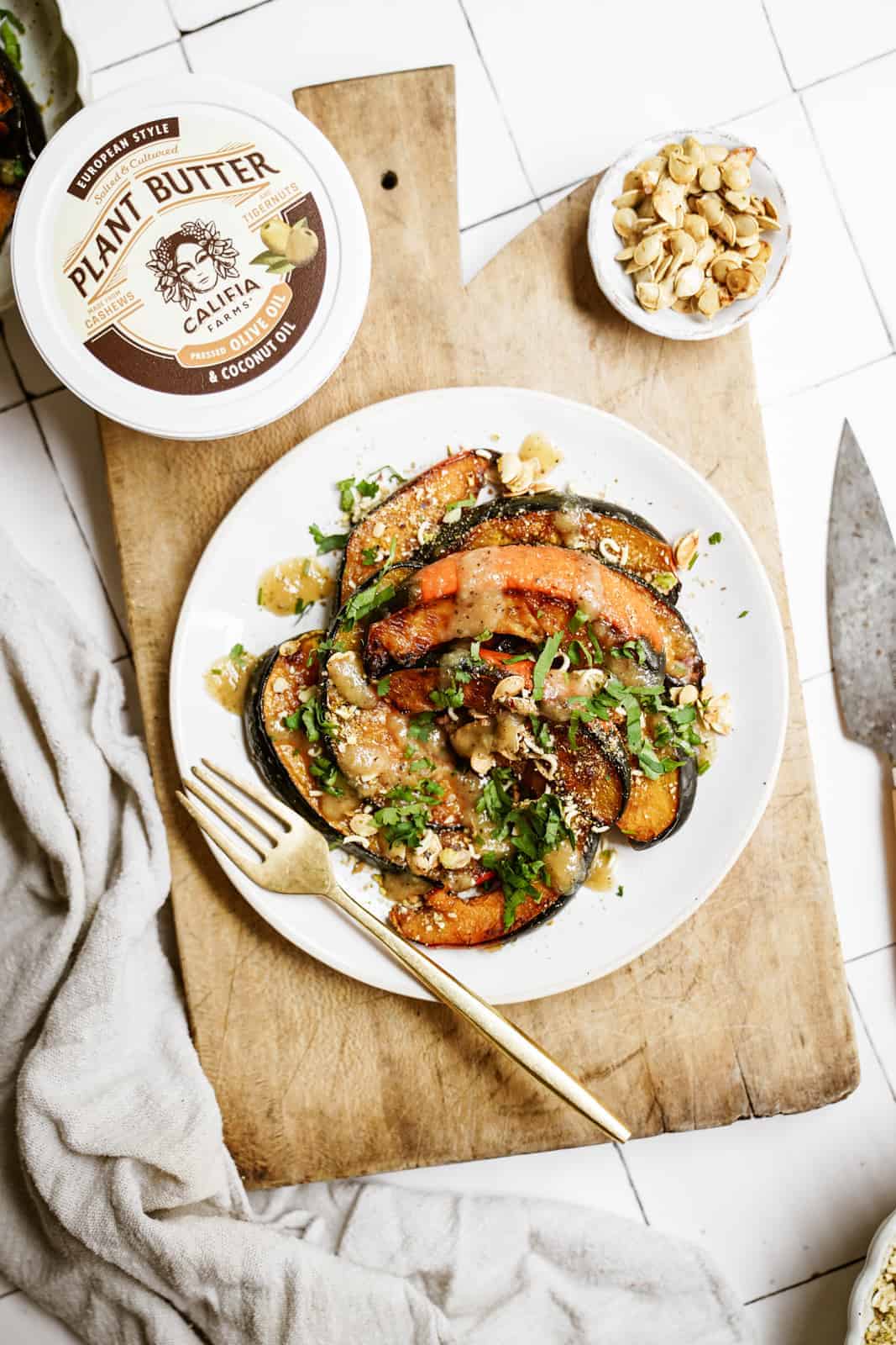Roasted acorn squash recipe on a white plate on a cutting board with Califia Farms Plant Butter