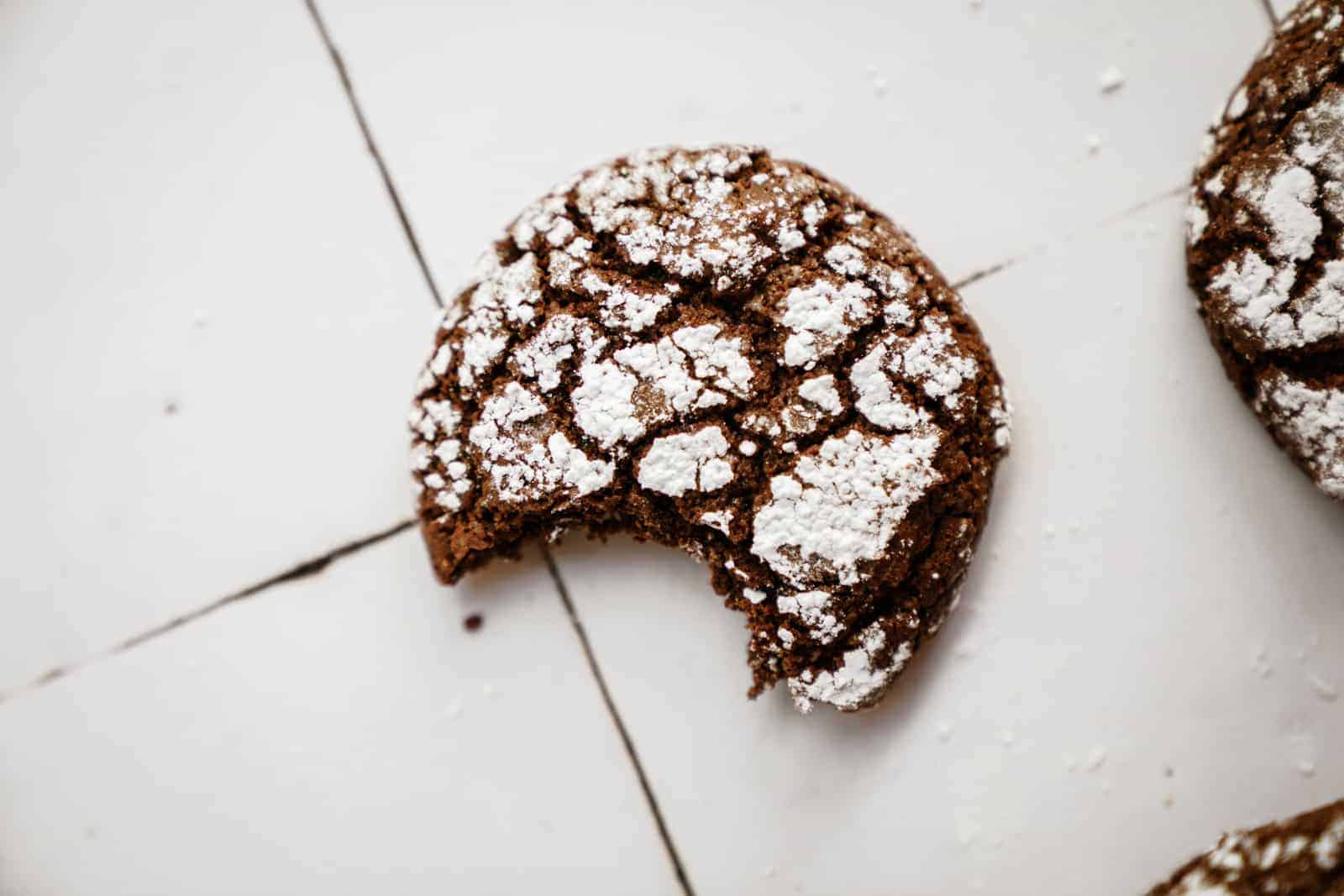 This Chocolate Crinkle Cookie Recipe is to die for. Cookie on white counter with bite out of it.