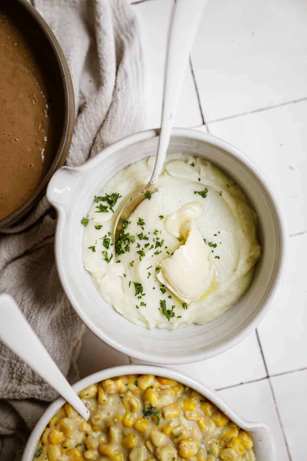 Vegan Mashed Cauliflower in a bowl with butter on top, next to creamed corn.