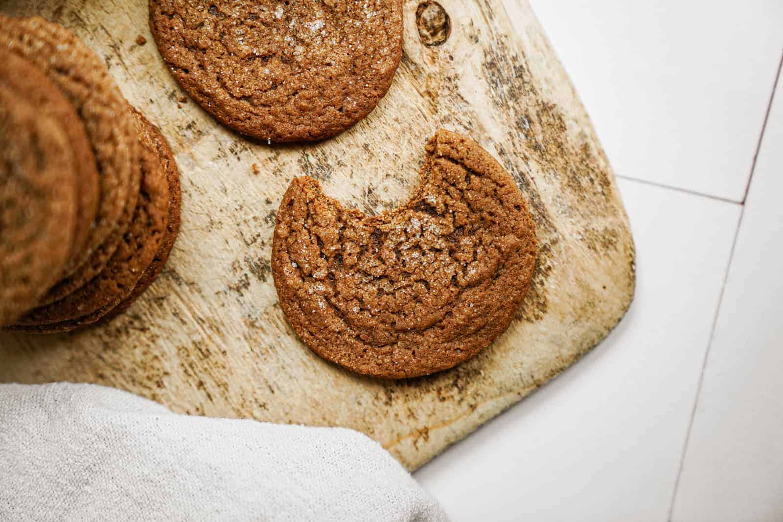 Vegan Ginger Snap Cookies on a cutting board with a bite out of one.