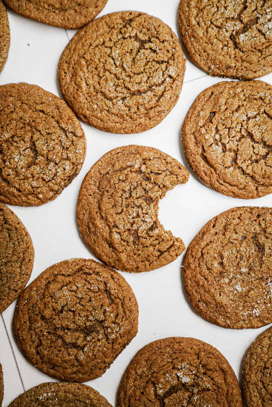Vegan Ginger Snap Cookies laying on a white surface with one missing a bite out of it.
