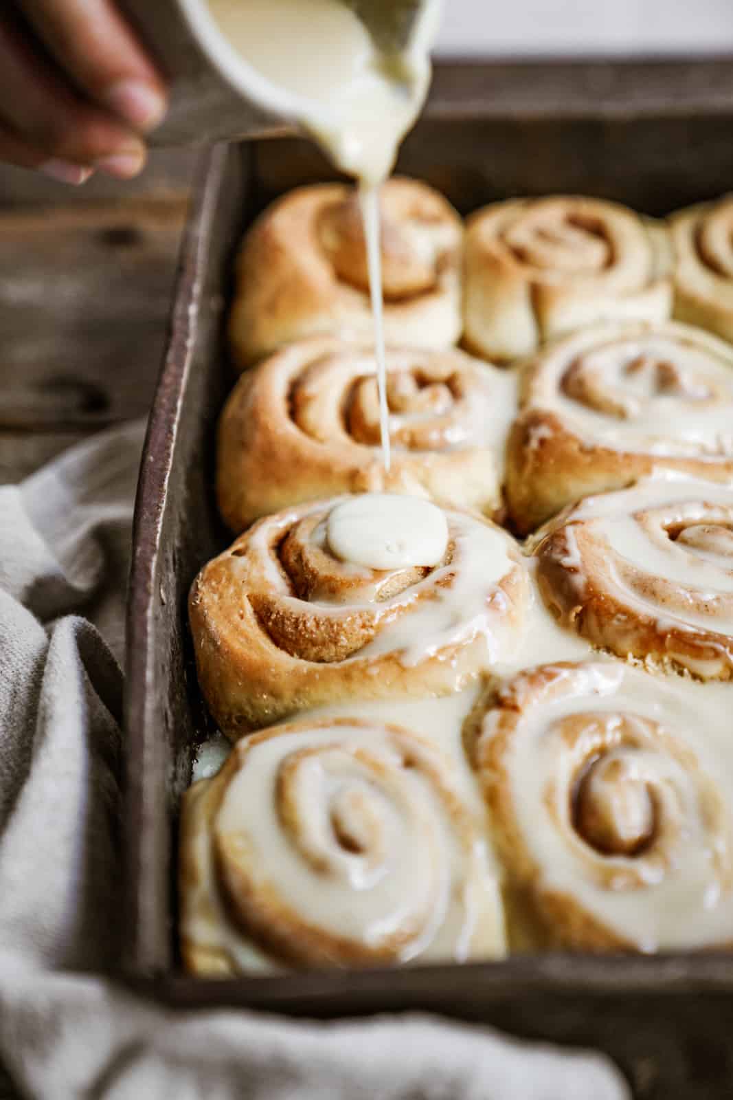 Icing being poured on Vegan Cinnamon Buns