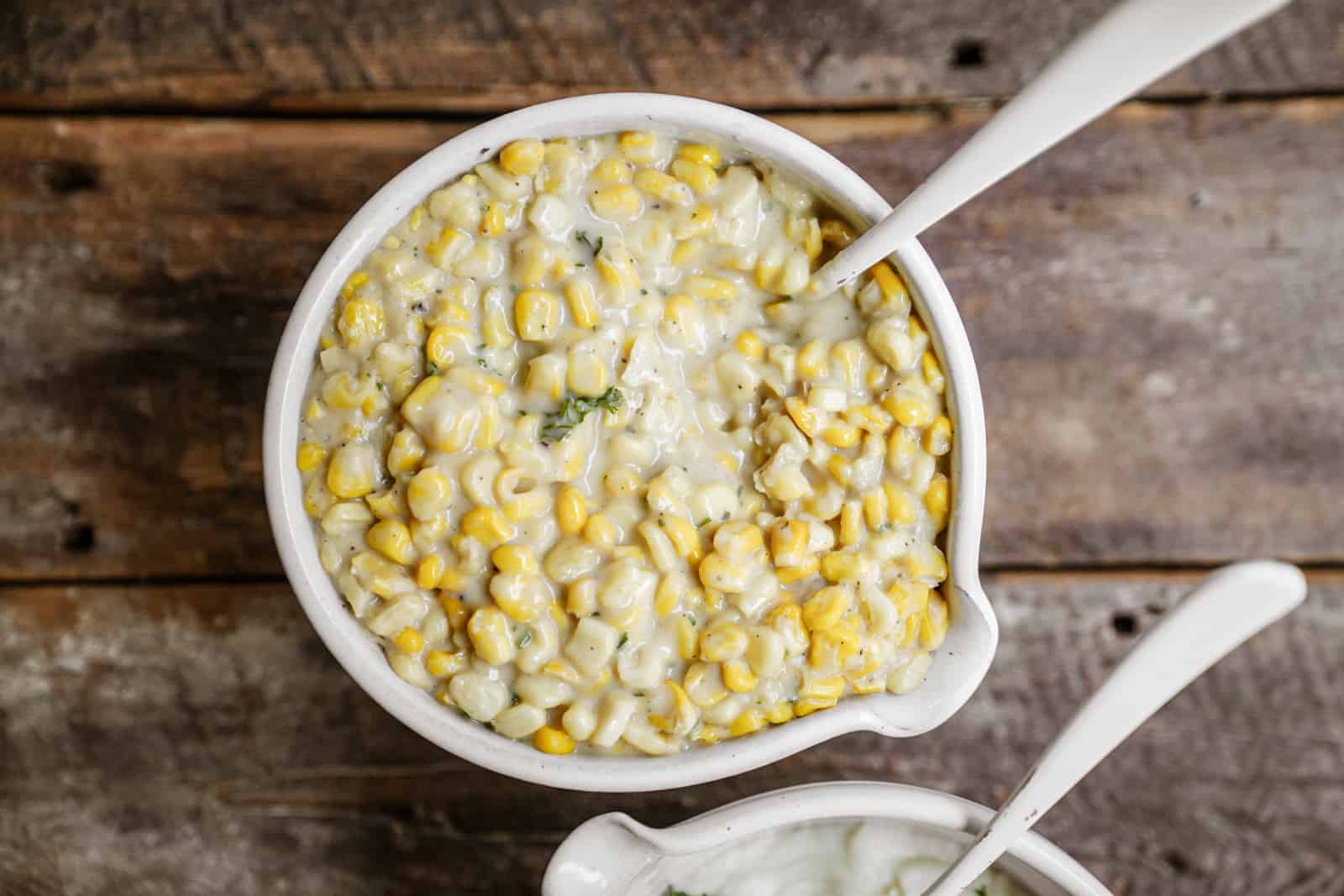 Creamed corn recipe in a serving dish on a wooden countertop.