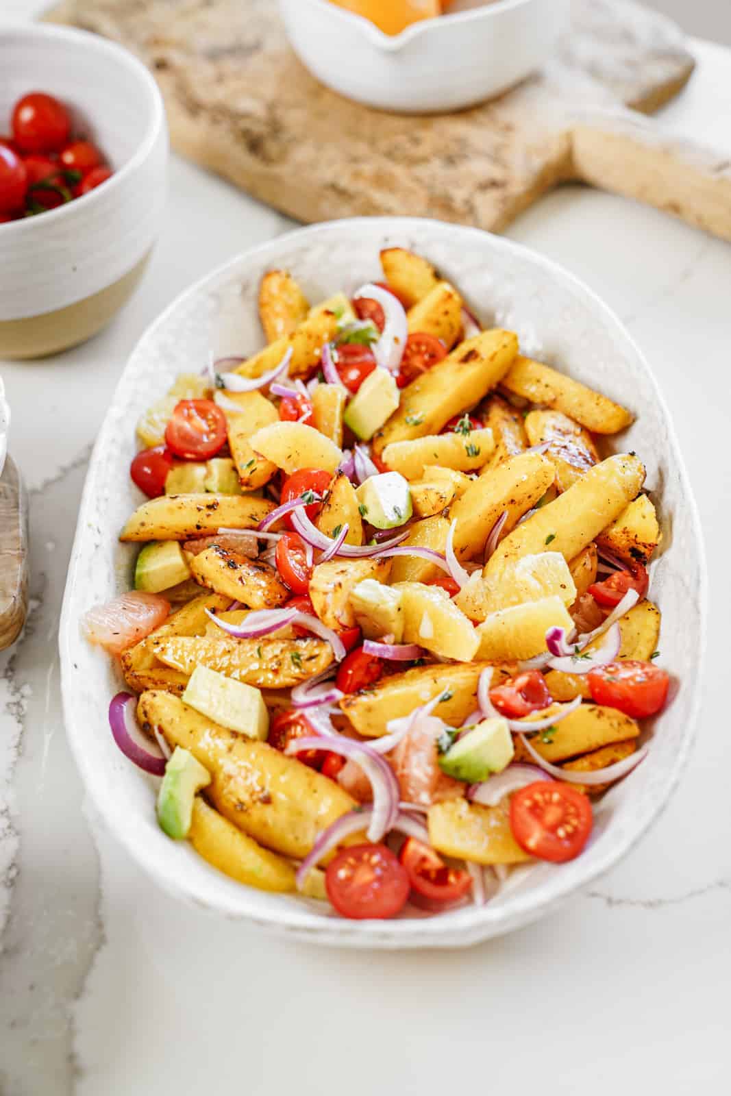 Big serving dish of vegan roasted potato salad with fresh veggies and citrus flavor.