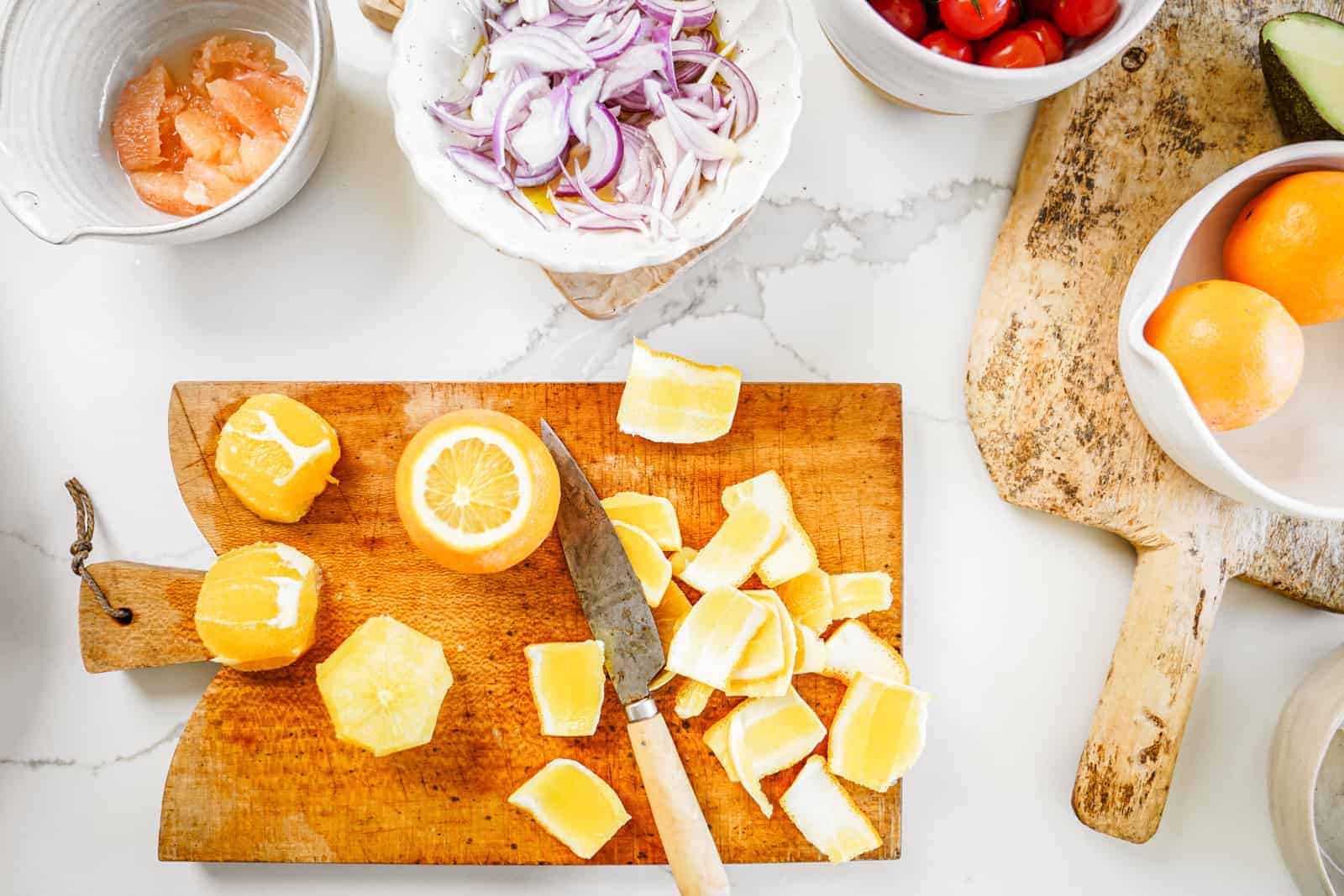 Cutting board of oranges being cut, surrounded by bowls of ingredients for roasted potato salad.