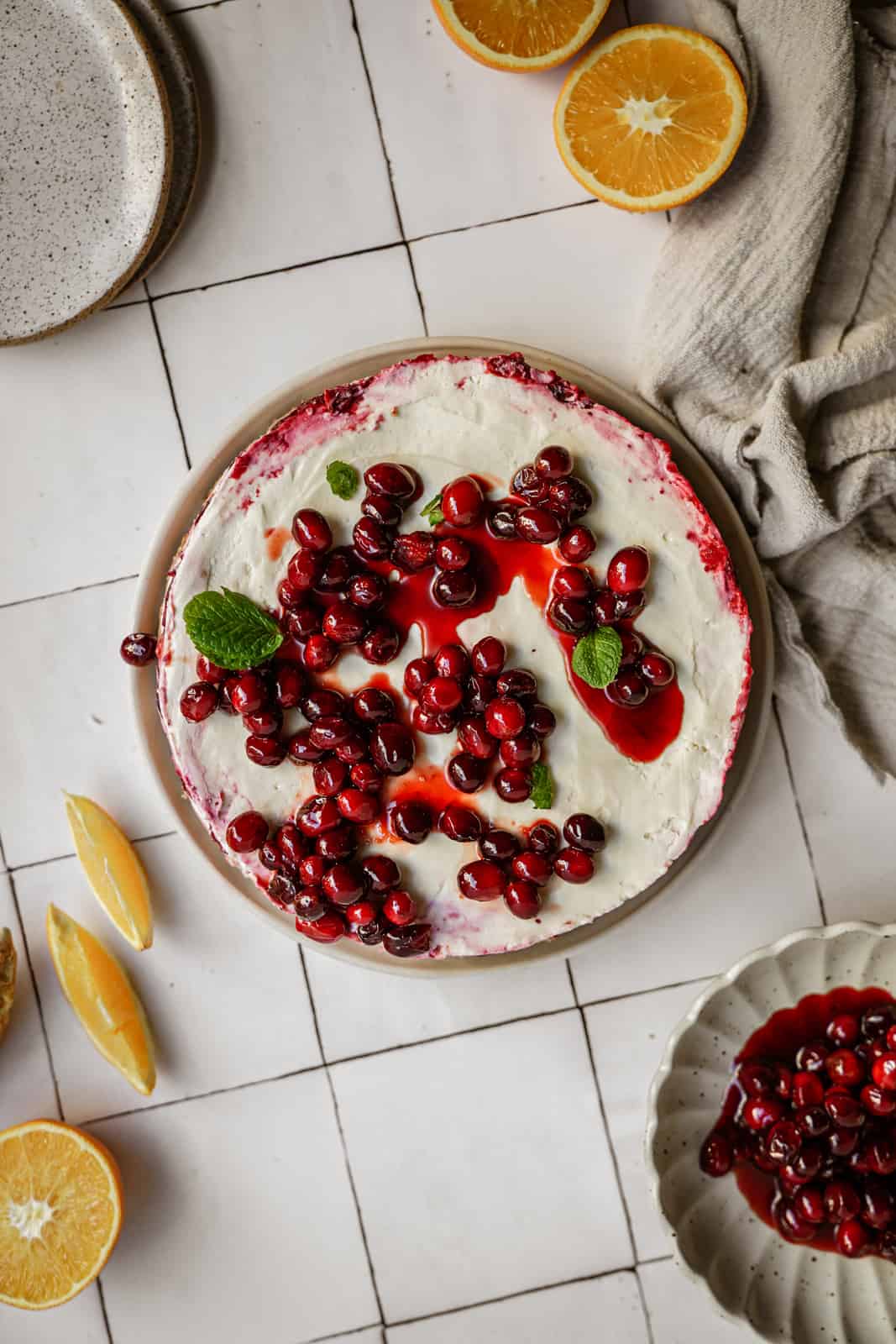 No-bake vegan cheesecake with cranberries on top, surrounded by oranges on countertop.