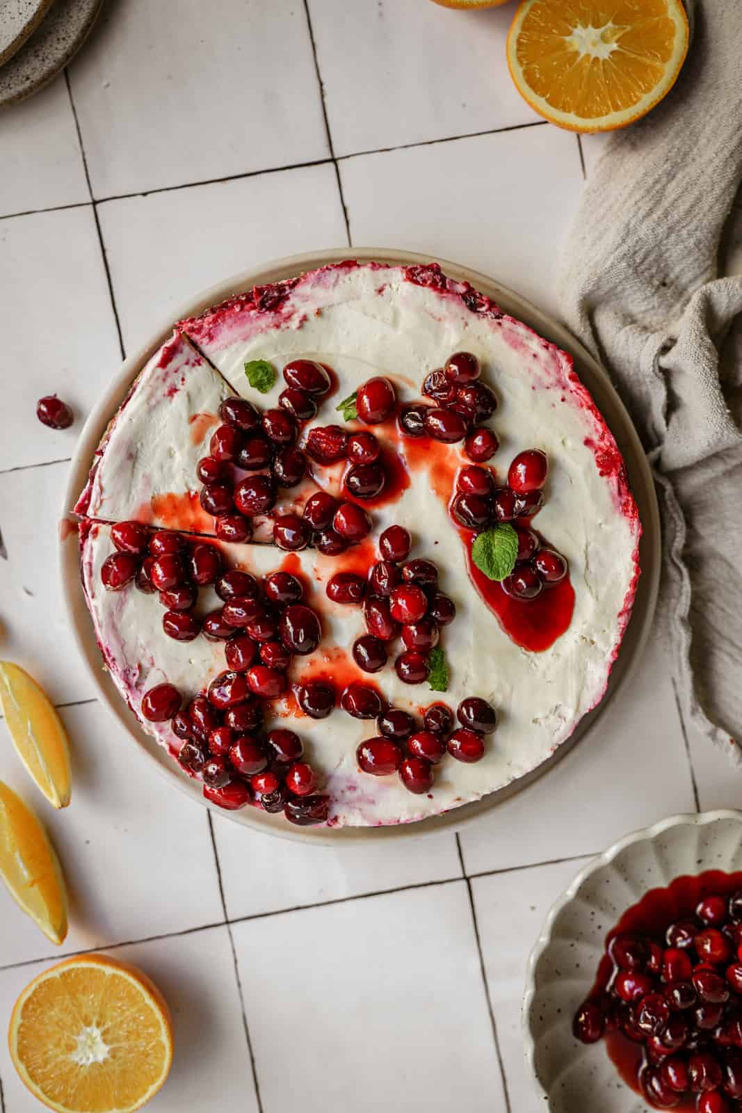 No-bake vegan cheesecake with cranberries and raspberries on top, surrounded by oranges on counter.