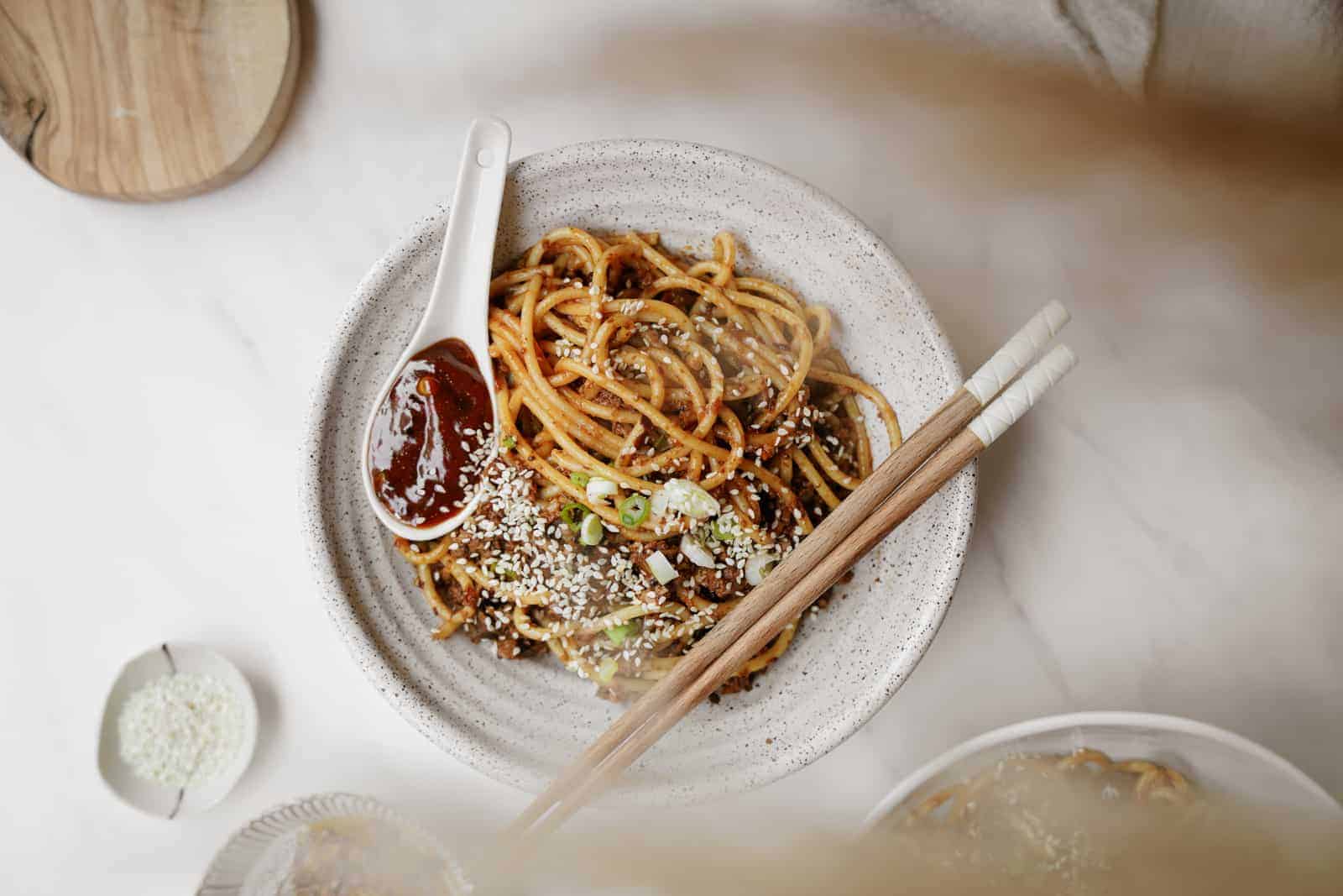 Vegan dan dan noodles in a white bowl with chopsticks.