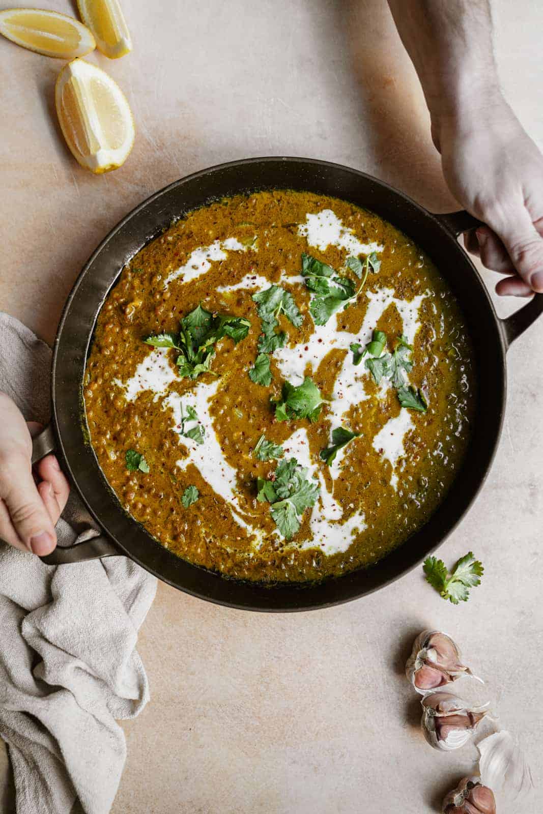 green lentil recipe in a serving dish with two hands holding it.