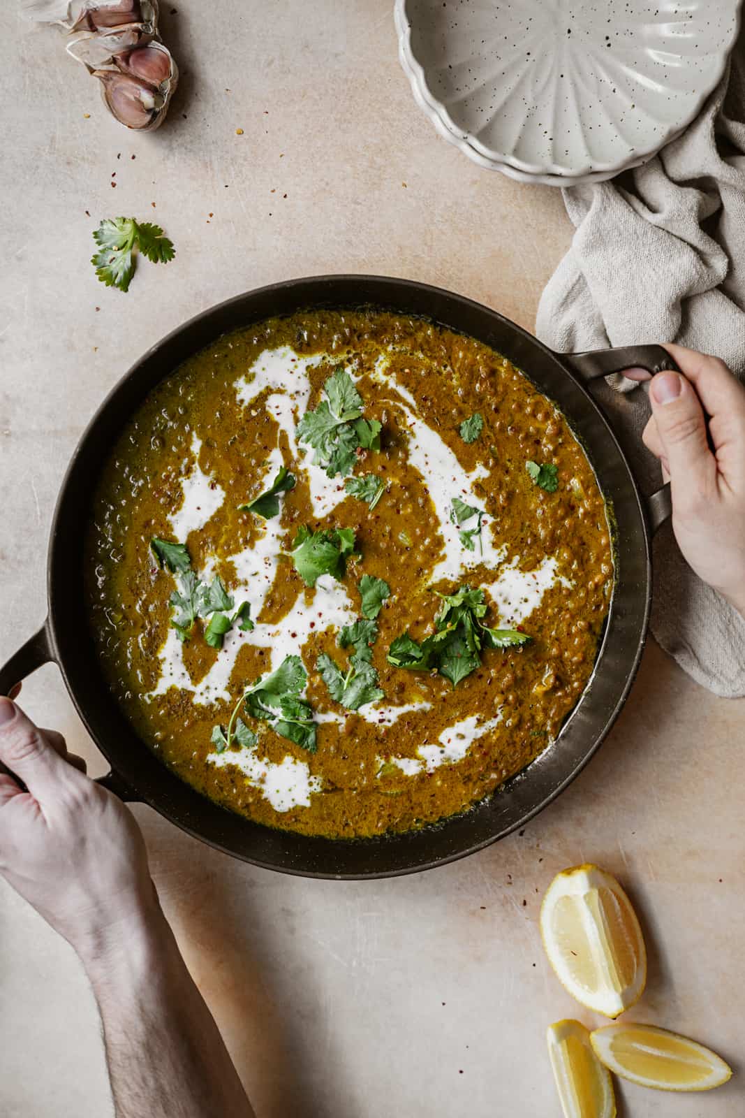 Green Lentil Curry in a serving dish with two hands holding it.