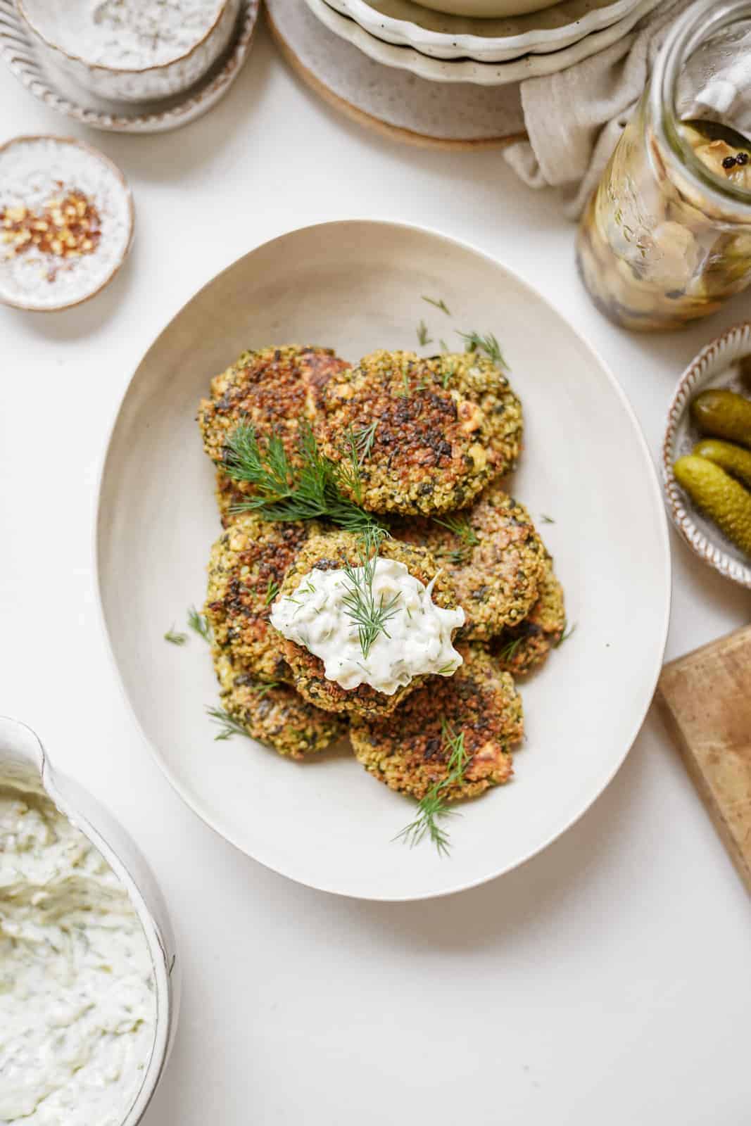Quinoa and Spinach Patties on serving dish on countertop surrounded by ingredients.