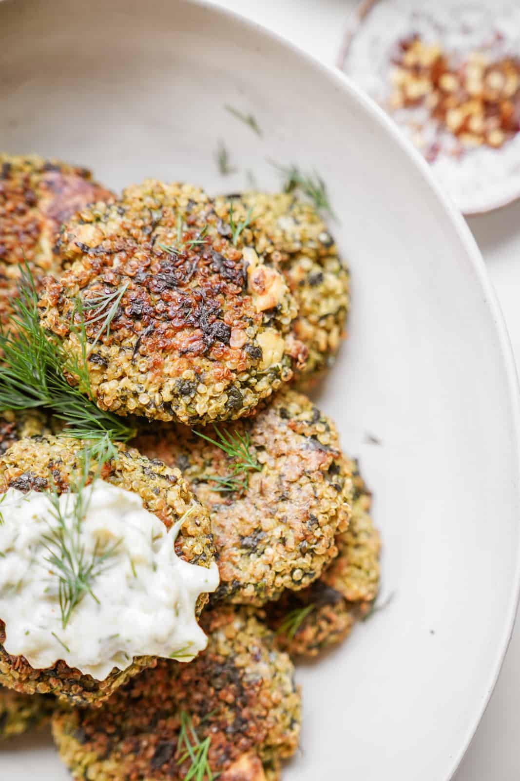 Close up of quinoa and spinach patties in serving dish topped with aioli. 